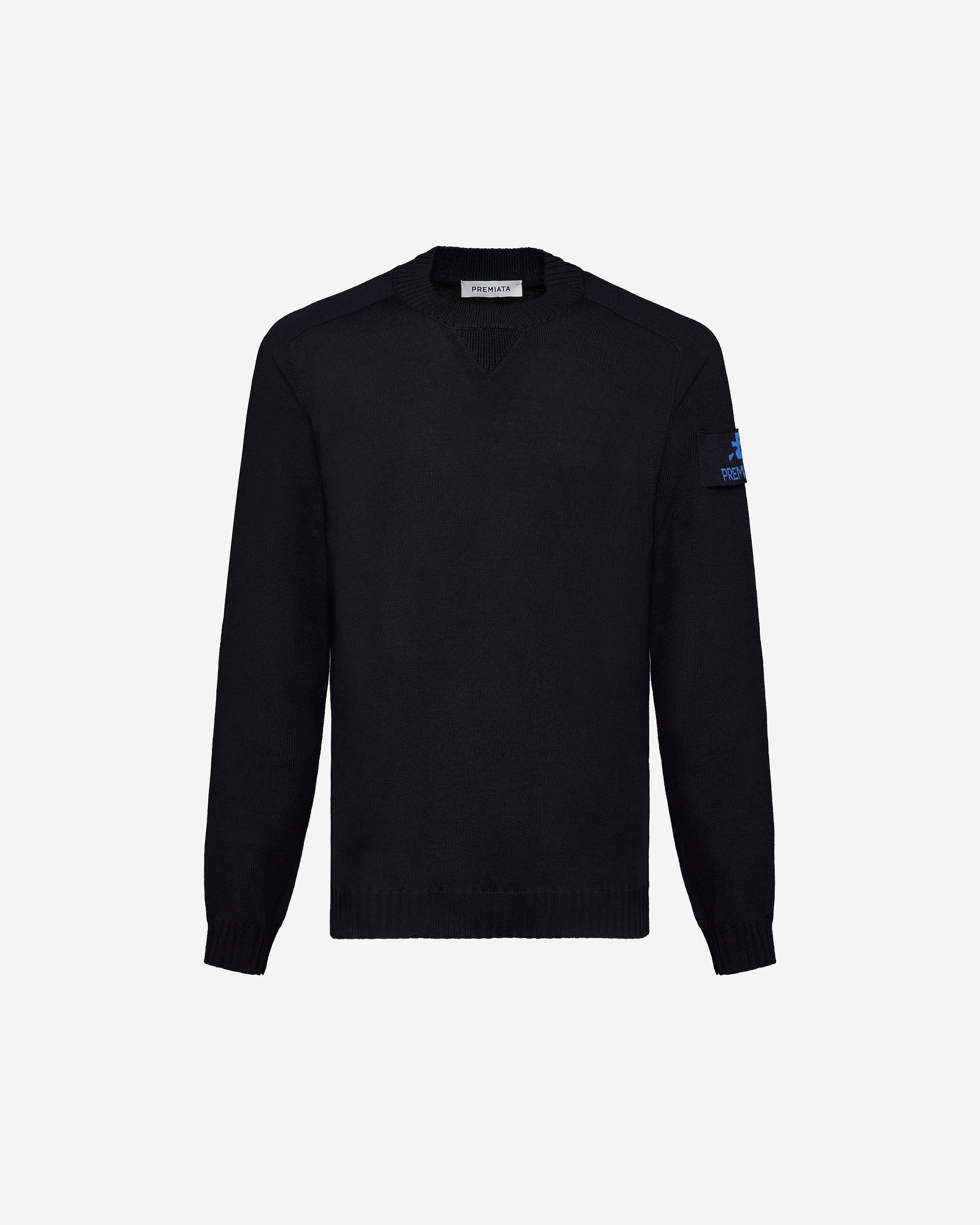 Maglione uomo blu scuro girocollo in lana merino, patch sul braccio sinistro, sfondo bianco.
