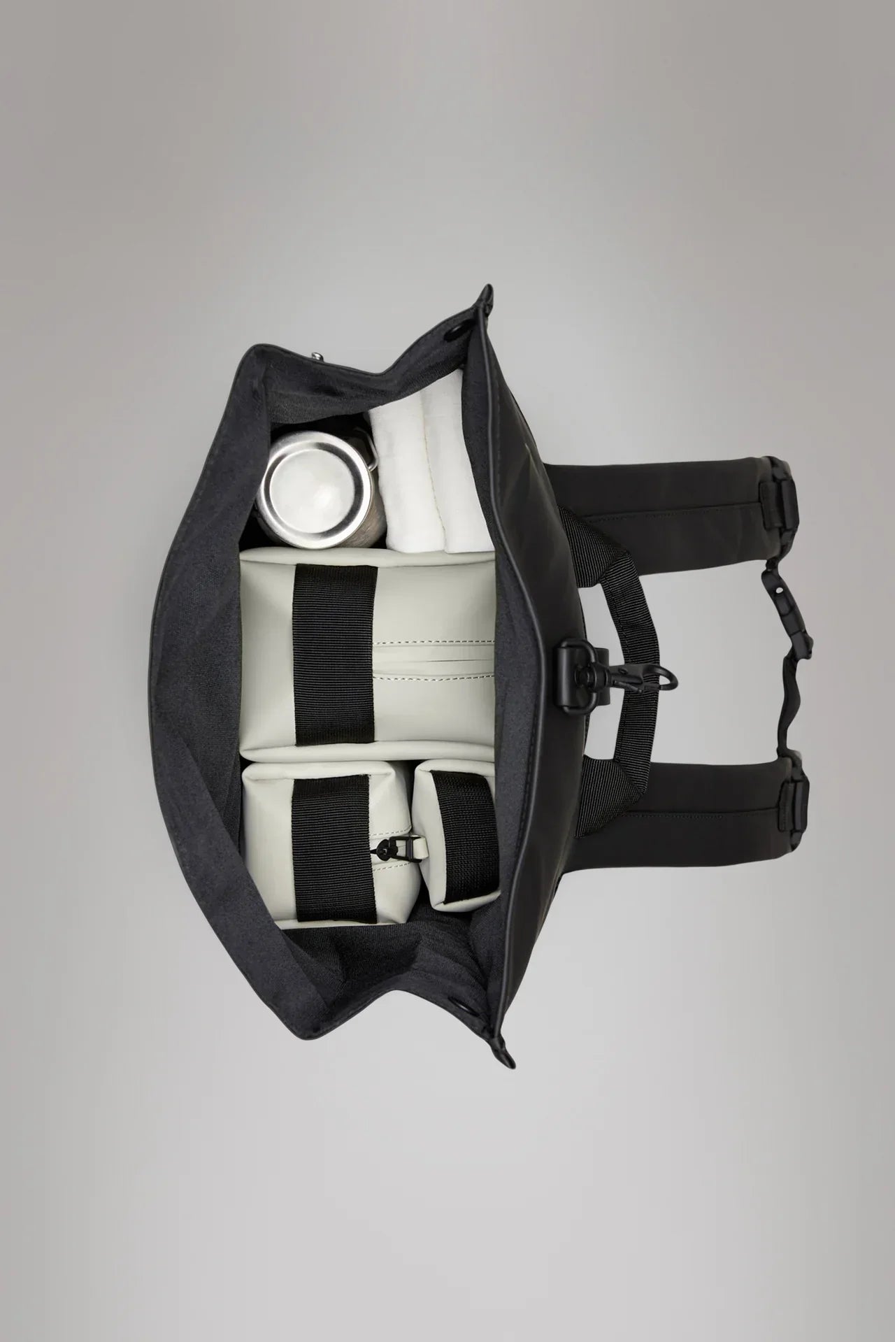 Zaino nero rolltop aperto visto dall'alto, interno organizzato con scomparti e oggetti riposti