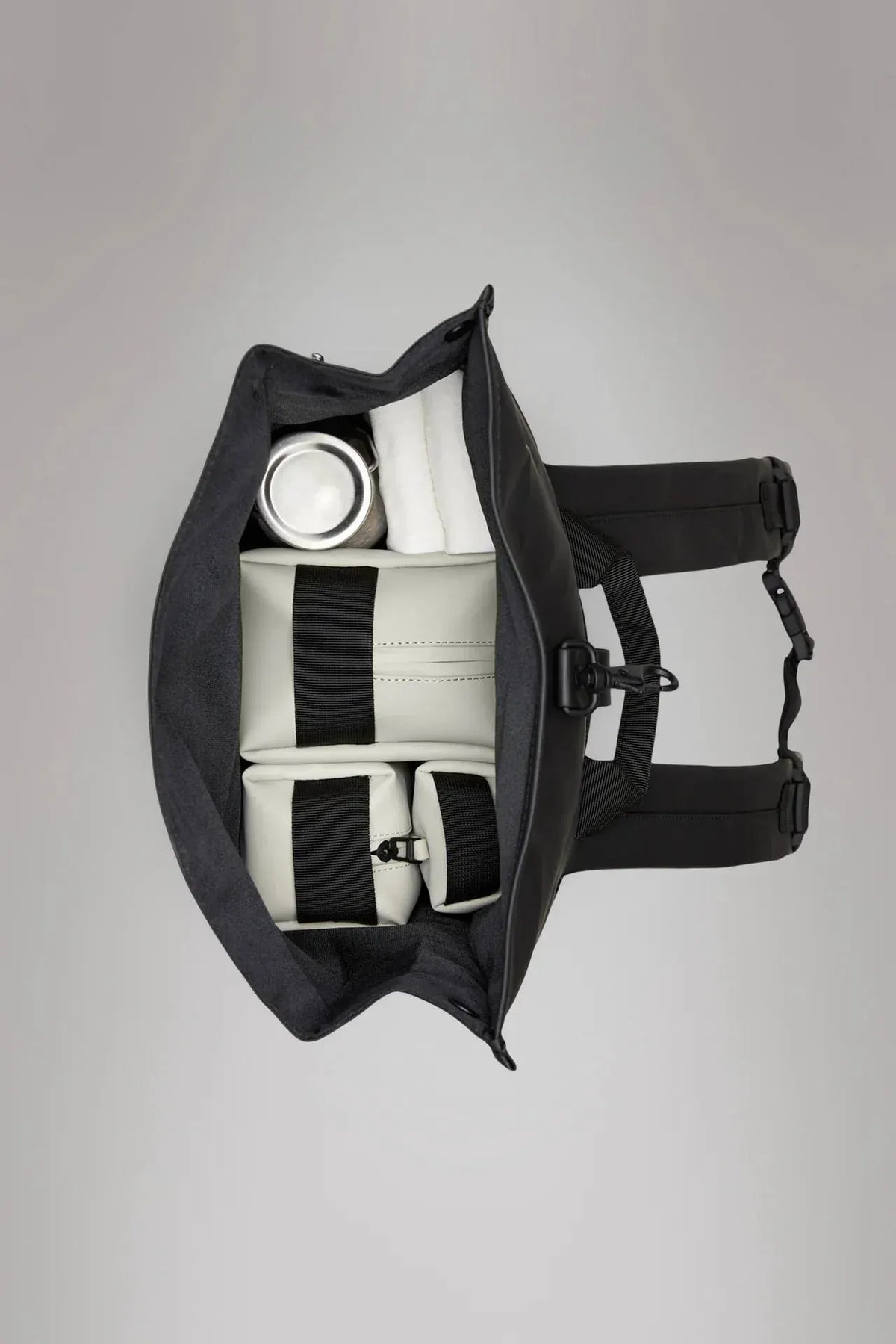 Zaino nero rolltop aperto visto dall'alto, interno organizzato con scomparti e oggetti riposti