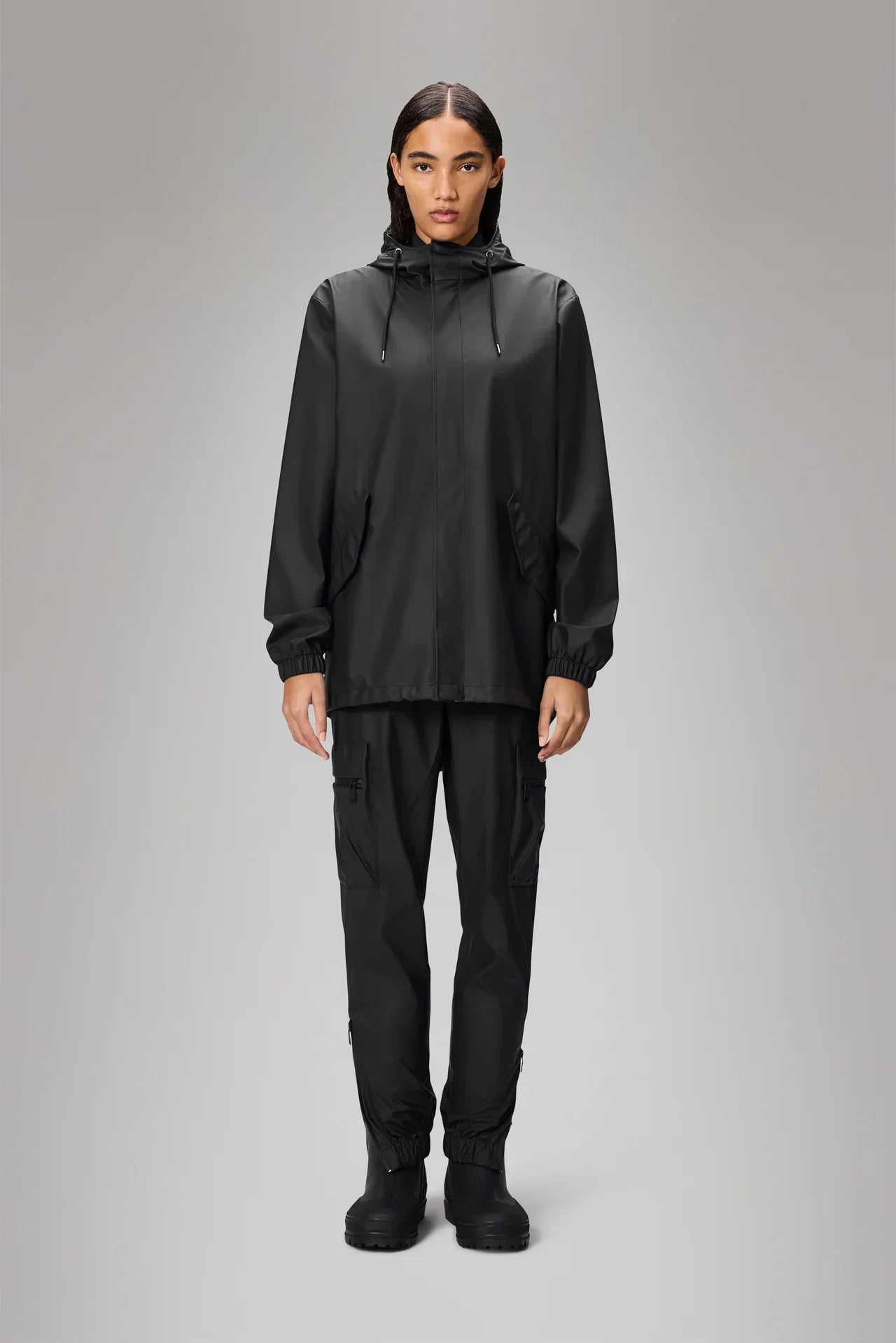 Donna con giacca antipioggia nera con cappuccio e pantaloni cargo neri in stile casual