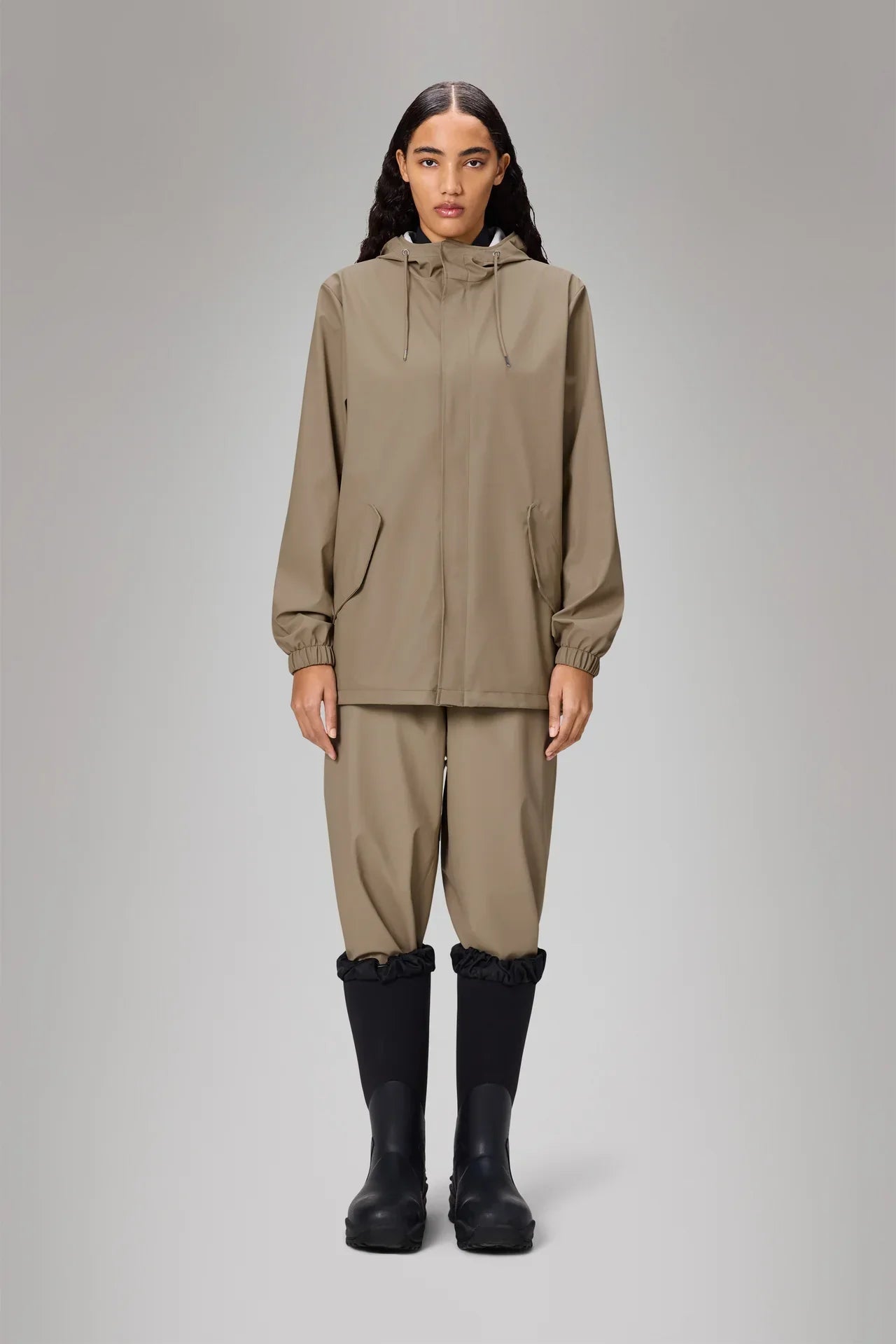 Giacca impermeabile beige da donna con cappuccio, pantaloni abbinati e stivali neri