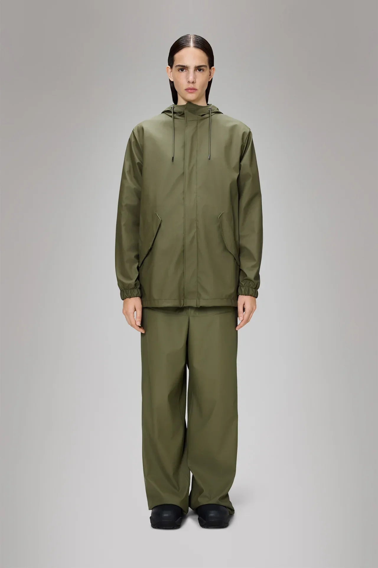Modello indossa giacca antipioggia verde oliva con cappuccio e pantaloni coordinati, abbigliamento impermeabile uomo donna