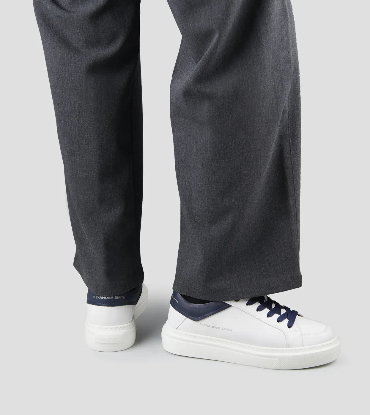 Sneakers uomo in pelle bianca con dettagli blu e pantaloni grigi, stile casual elegante