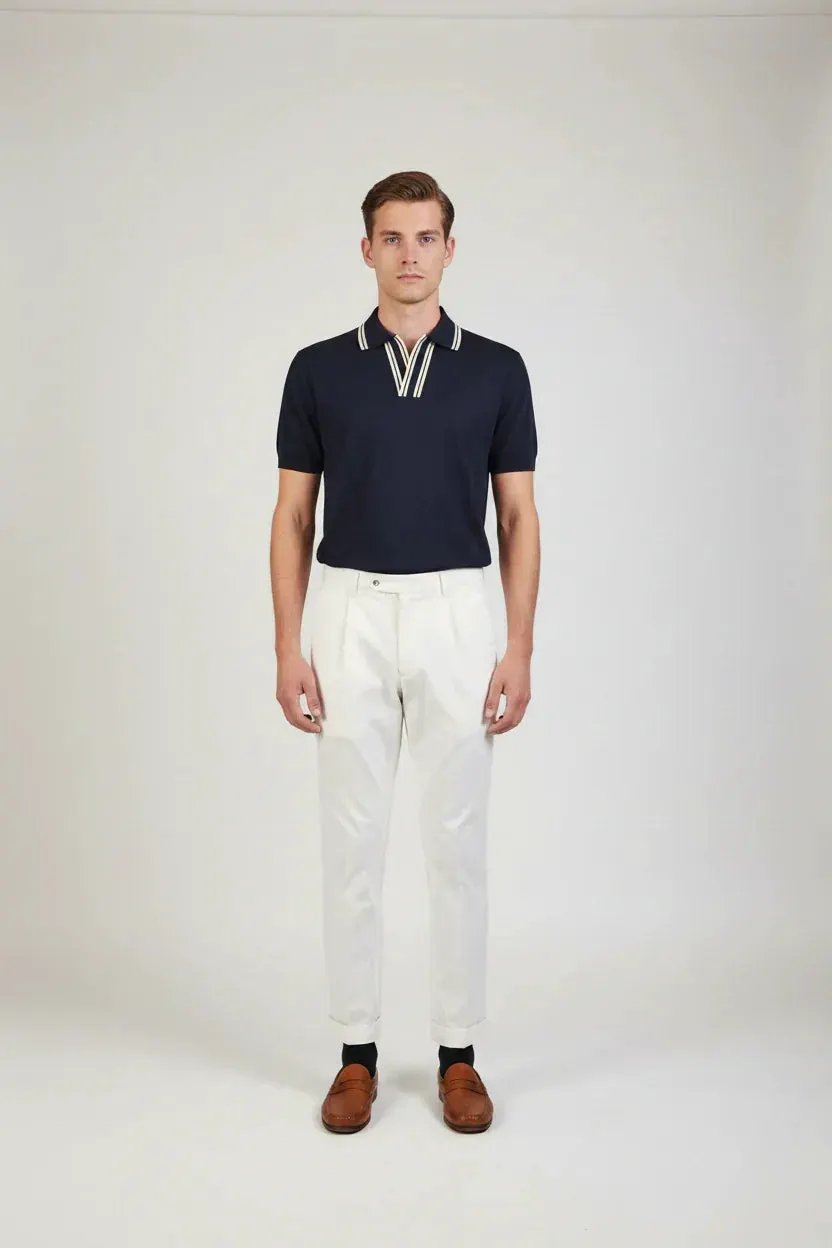 Uomo con polo blu scuro a maniche corte e pantaloni bianchi eleganti, look moda uomo.