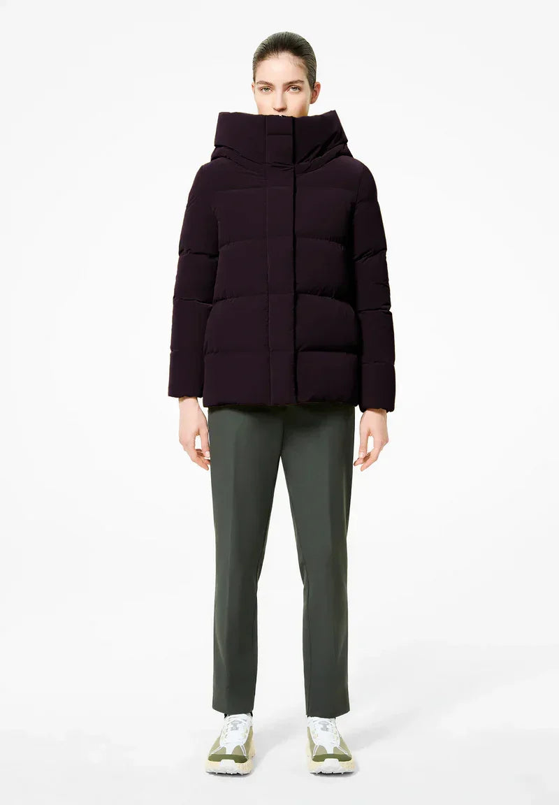 Donna con piumino bordeaux imbottito e cappuccio alto, pantaloni verdi e sneakers chiare