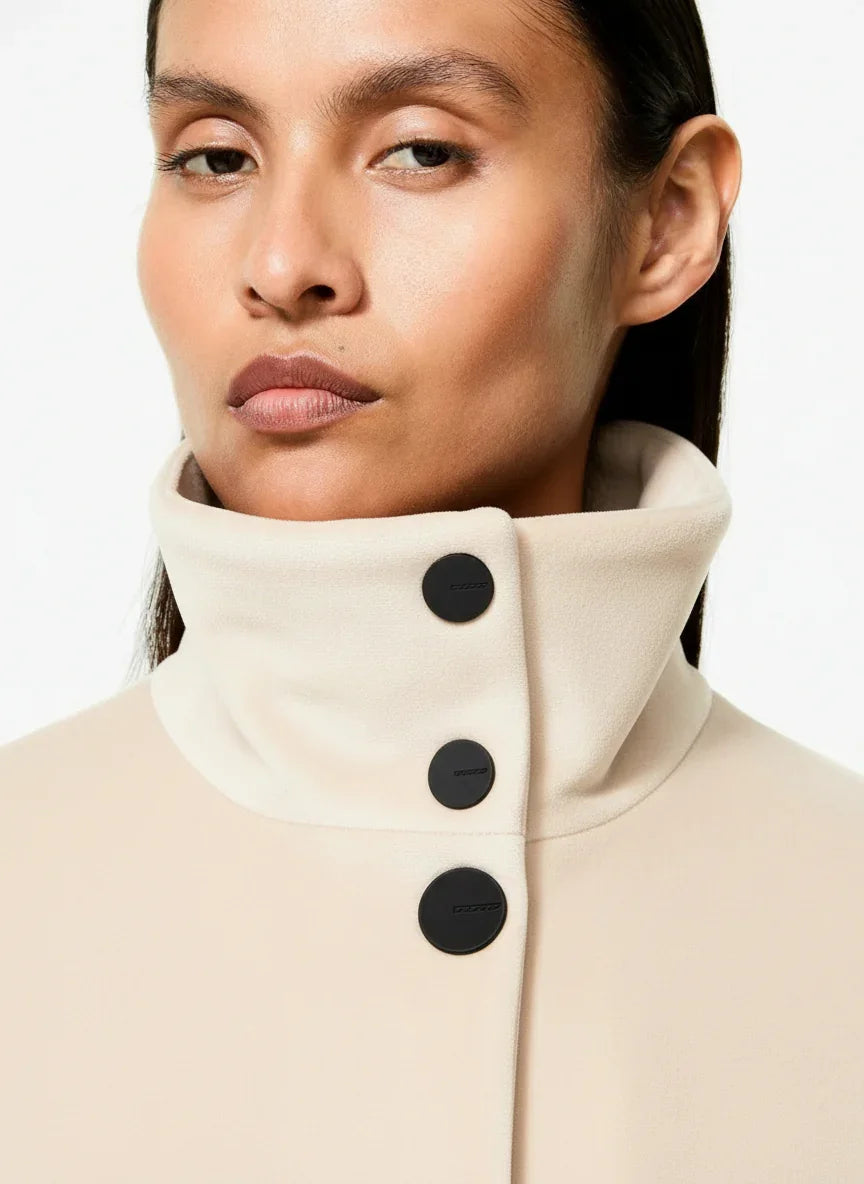 Cappotto donna beige elegante con collo alto e bottoni neri opachi, dettaglio primo piano.
