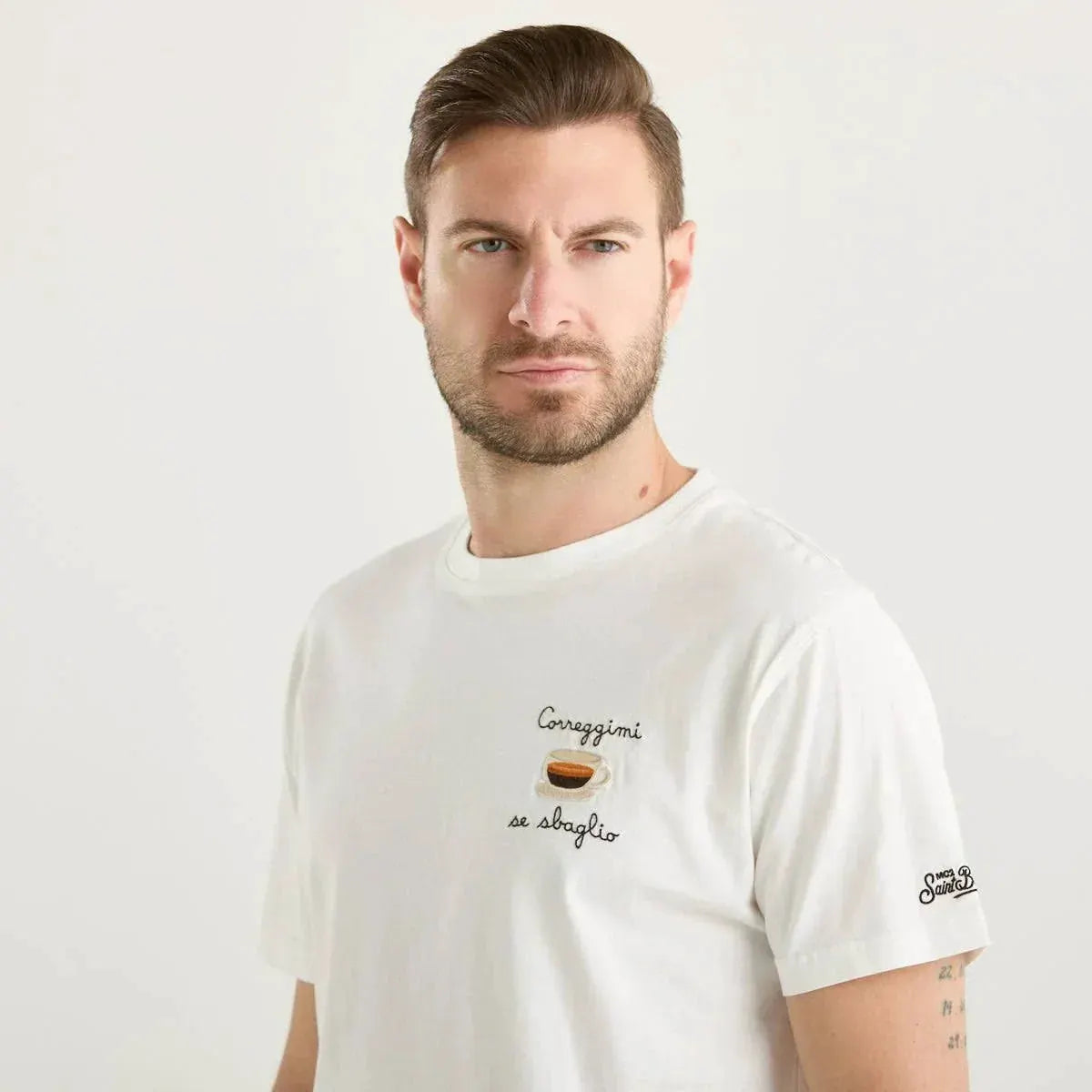 Uomo con t-shirt bianca, scritta 'Correggimi se sbaglio' e tazzina di caffè ricamata, moda casual uomo.