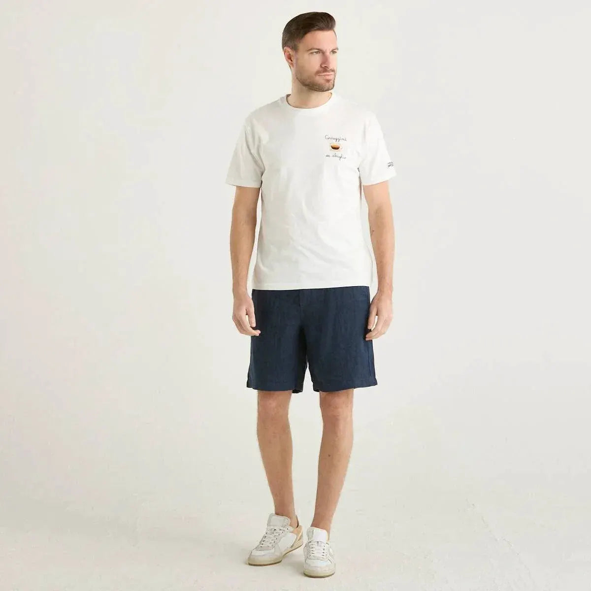 Modello indossa t-shirt bianca, bermuda blu navy e sneakers bianche, moda uomo casual.