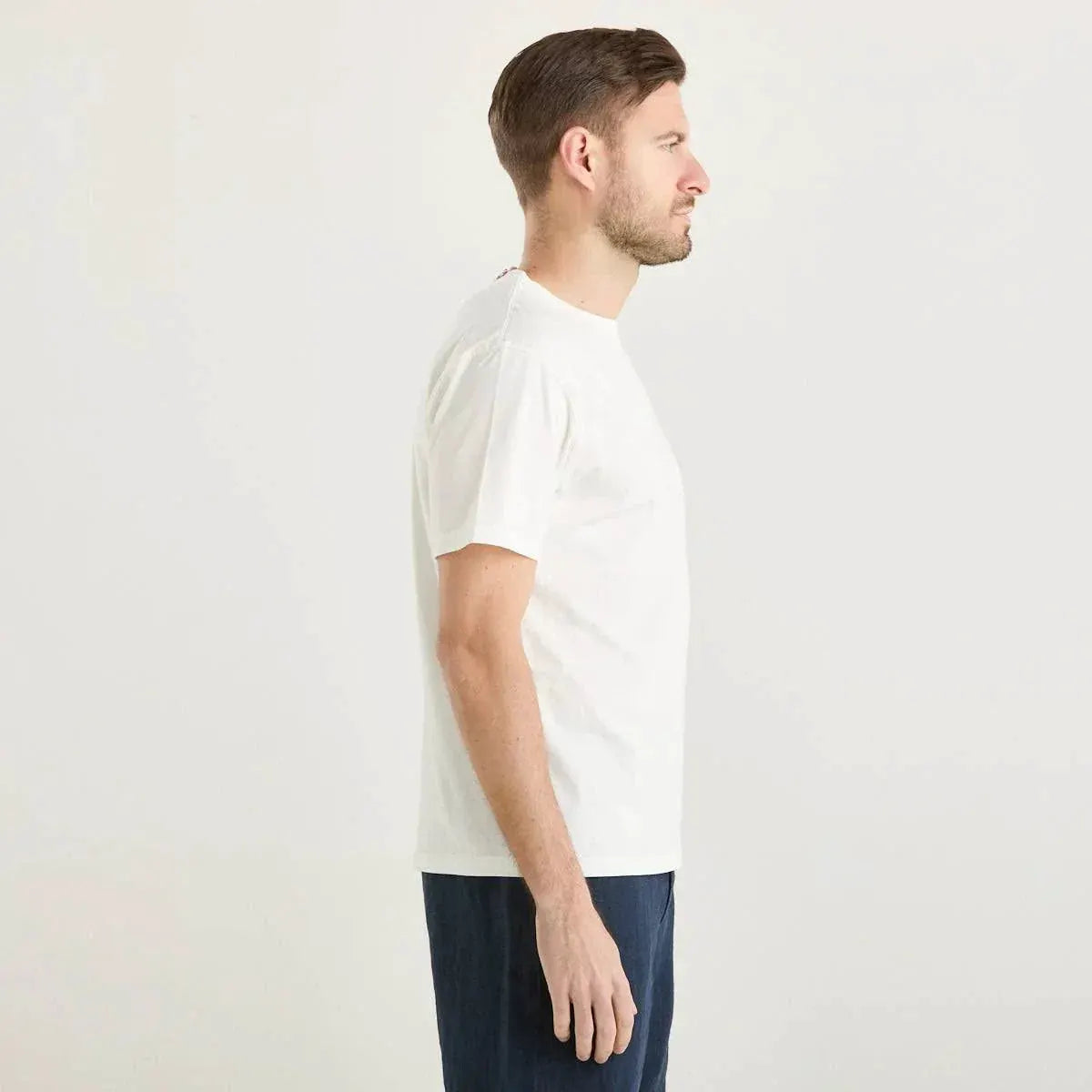 Uomo indossa t-shirt bianca basic e pantaloni blu, vista profilo, sfondo neutro