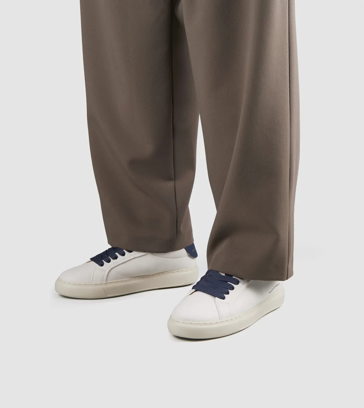 Sneakers uomo in nappa bianca con tallone blu e lacci blu, indossate con pantaloni marroni