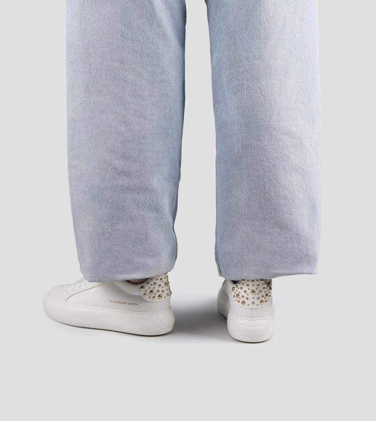 Sneakers donna bianche in pelle con borchie dorate, abbinate a pantaloni larghi chiari.