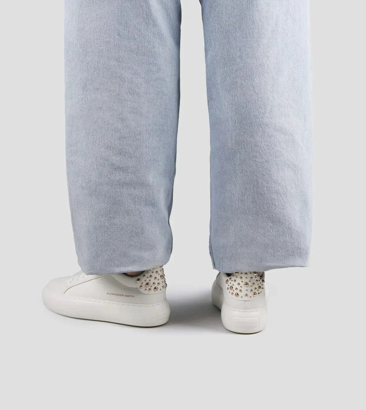Sneakers donna bianche in pelle con borchie dorate, abbinate a pantaloni larghi chiari.