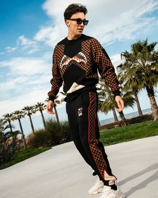 Uomo con felpa e pantaloni neri con dettagli marroni e rossi, look streetwear, all'aperto
