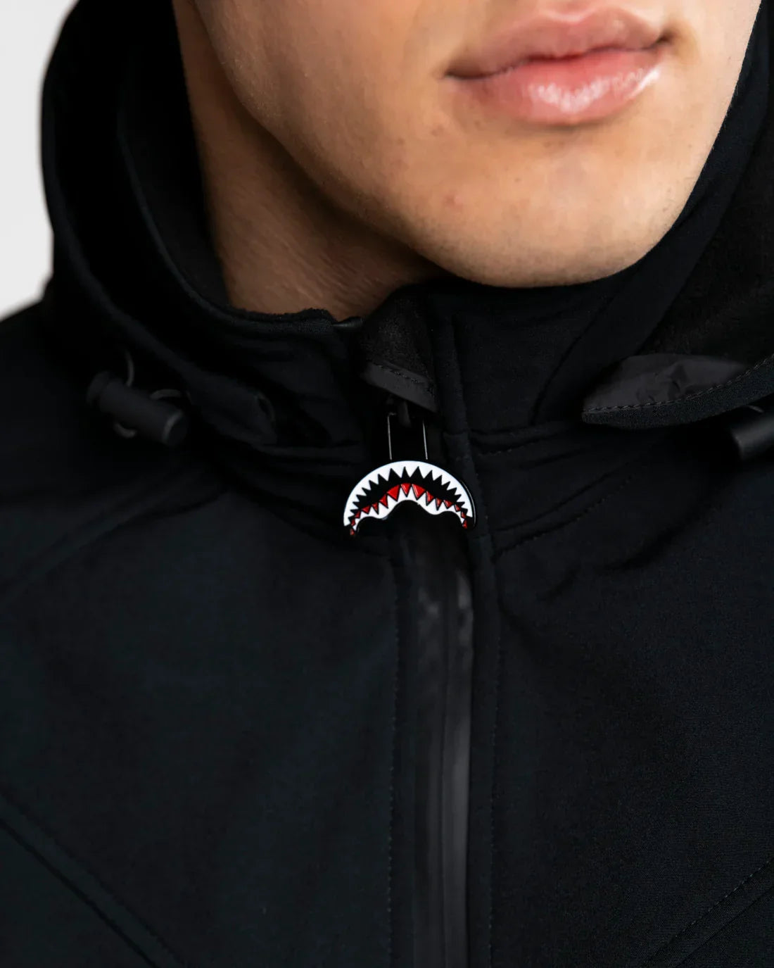 Dettaglio giacca nera da uomo con zip e cappuccio, tirazip motivo squalo