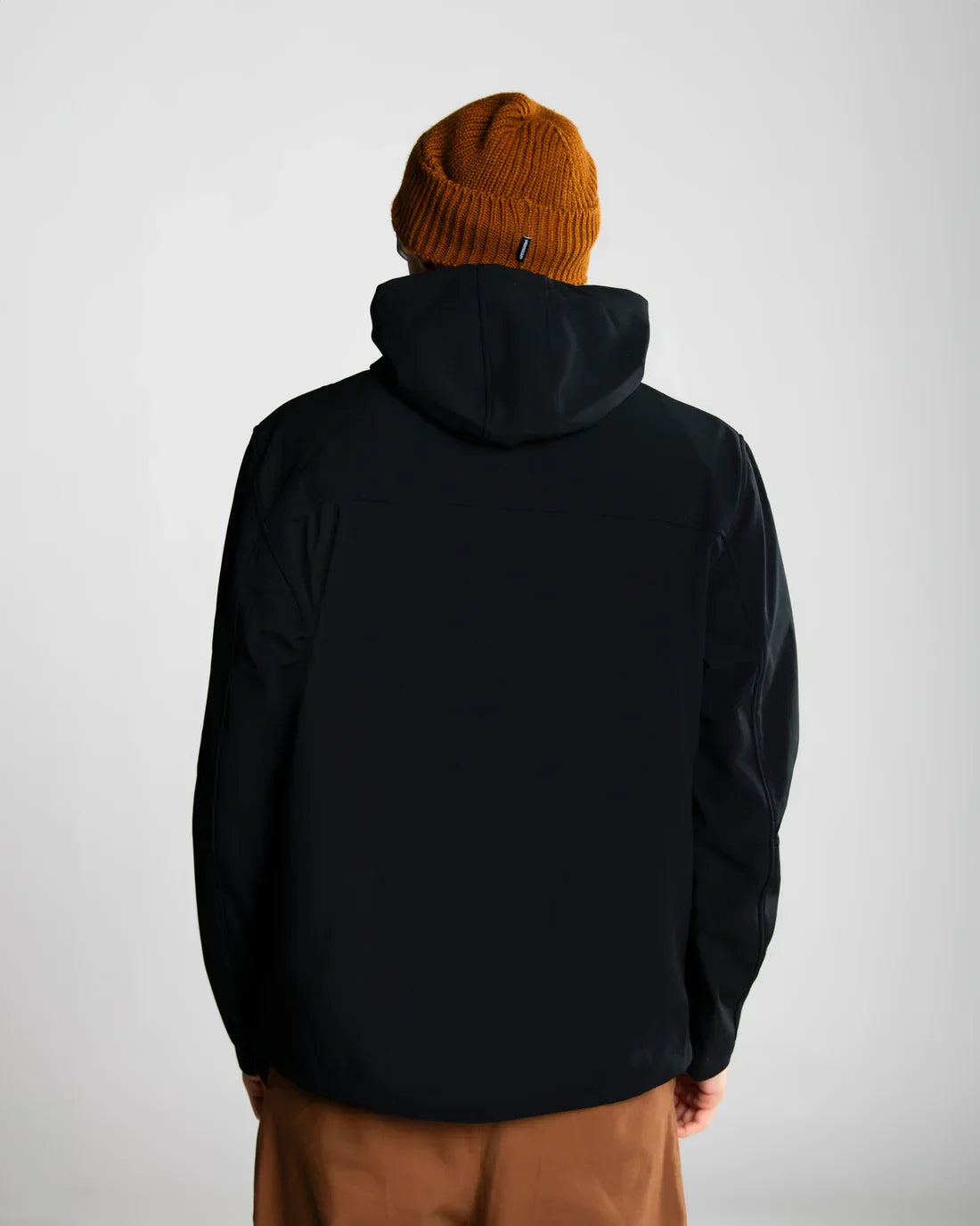 Giacca softshell nera da uomo con cappuccio vista posteriore, berretto arancione, pantaloni marroni
