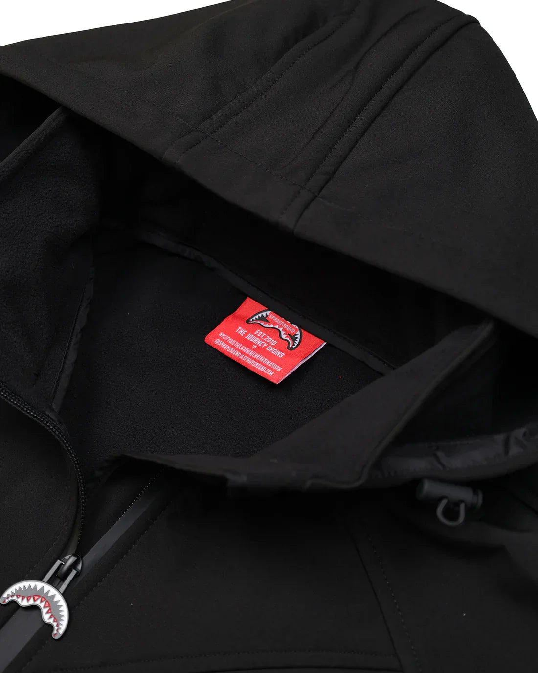 Giacca nera con cappuccio, dettaglio interno e zip decorativa con etichetta rossa visibile