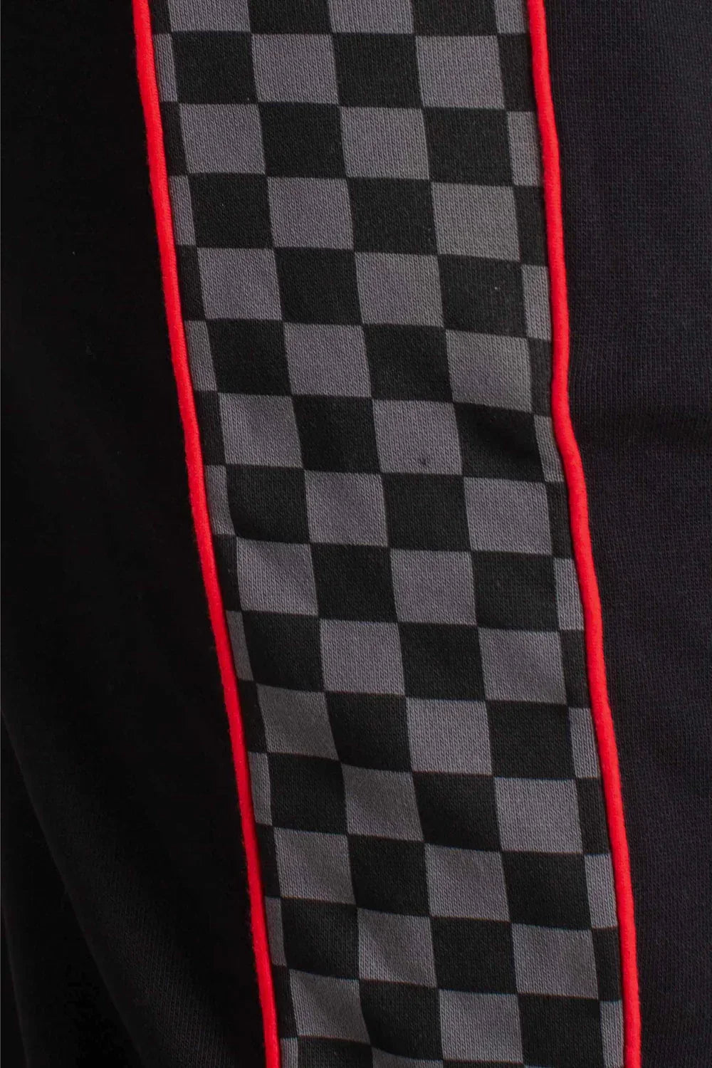 Dettaglio pantaloni neri con banda laterale a scacchi grigi e profili rossi, stile streetwear