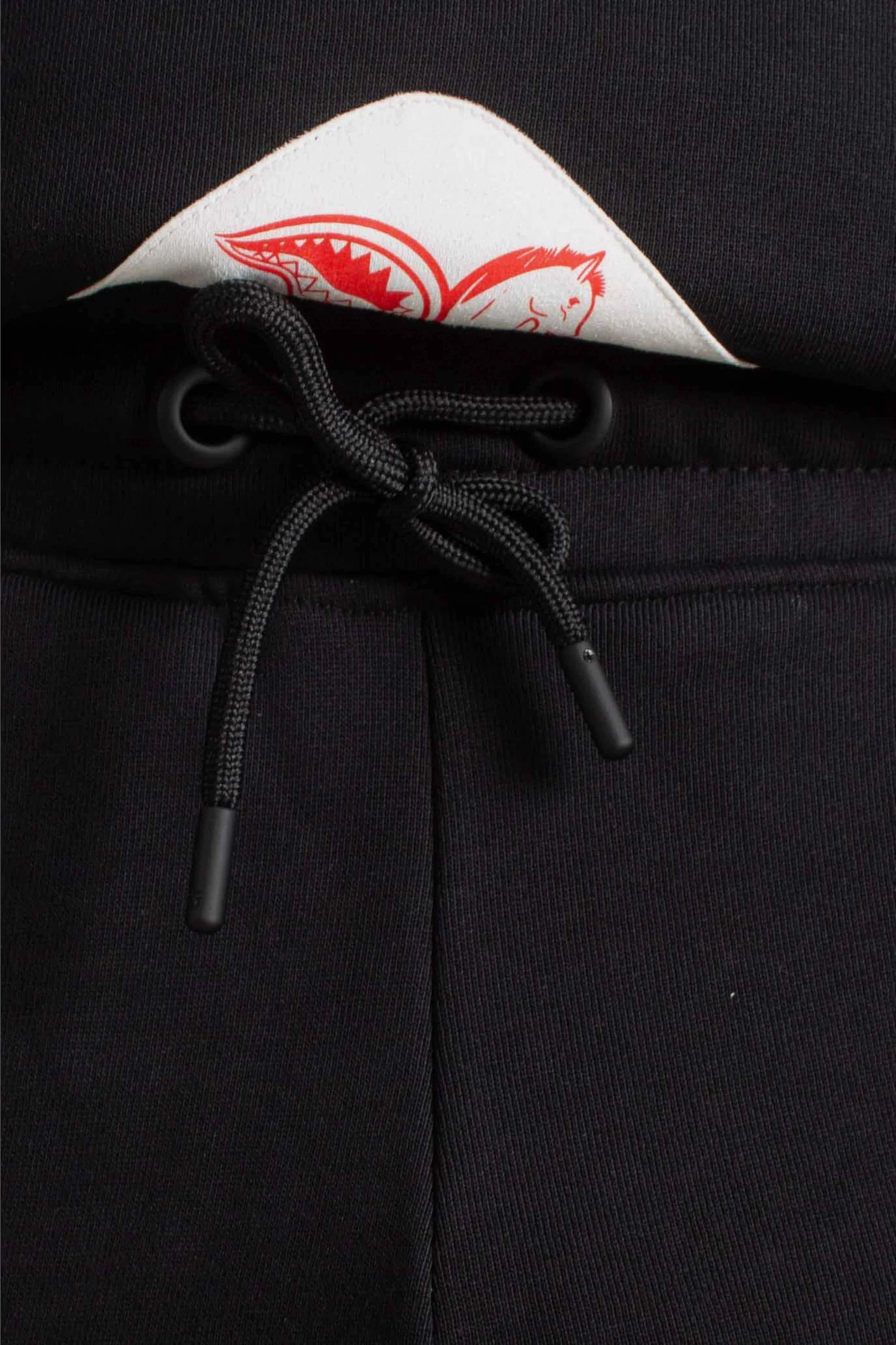 Dettaglio pantaloni grigi con coulisse nera e patch bianca stampata rosso, moda uomo.