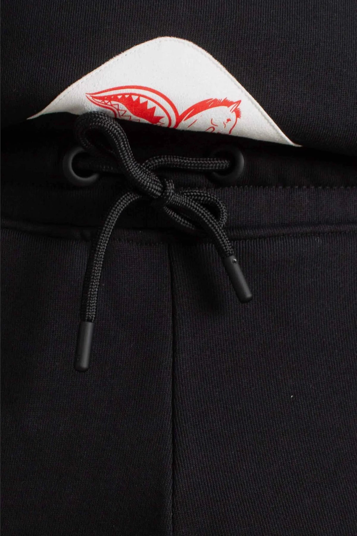 Dettaglio pantaloni grigi con coulisse nera e patch bianca stampata rosso, moda uomo.