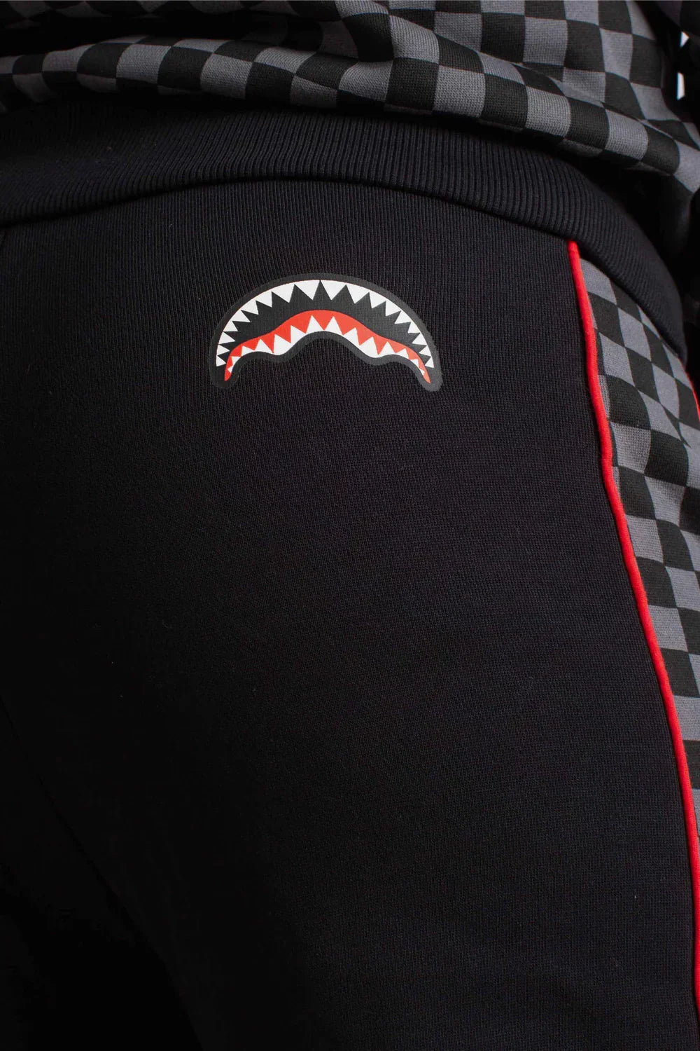 Pantaloni sportivi neri con dettagli a scacchi grigi, profilo rosso e stampa grafica di denti bianchi e rossi.