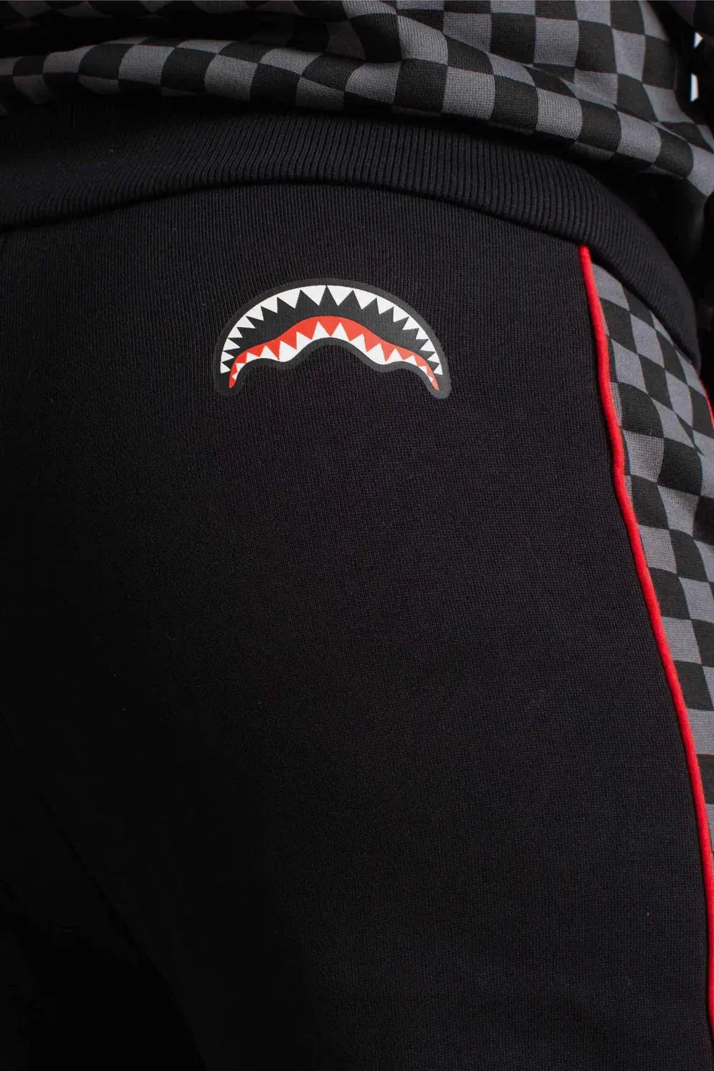 Pantaloni sportivi neri con dettagli a scacchi grigi, profilo rosso e stampa grafica di denti bianchi e rossi.