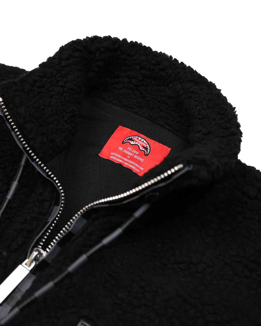 Giacca teddy nera in pile con zip e dettagli checkered, interno etichetta rossa visibile.
