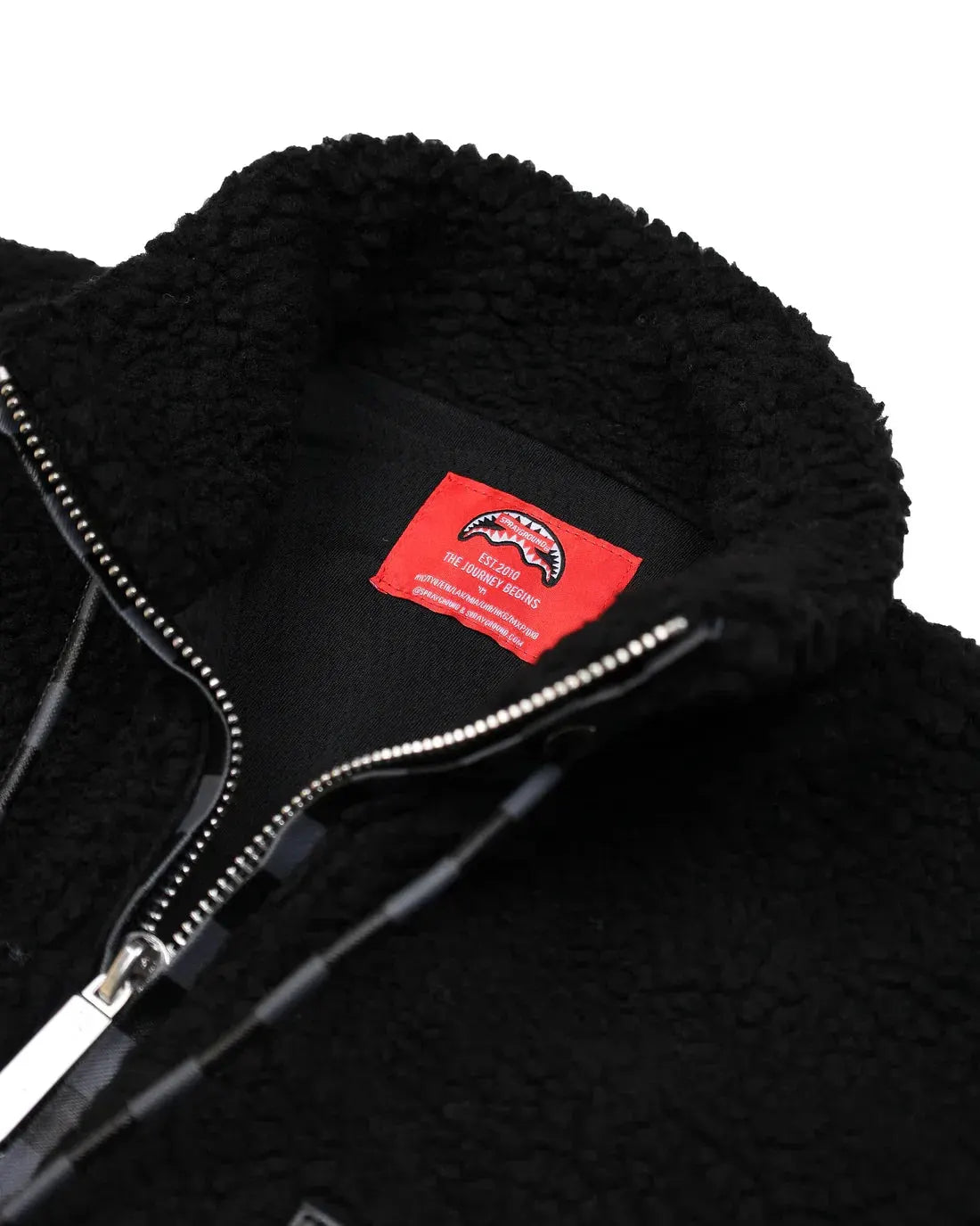 Giacca teddy nera in pile con zip e dettagli checkered, interno etichetta rossa visibile.