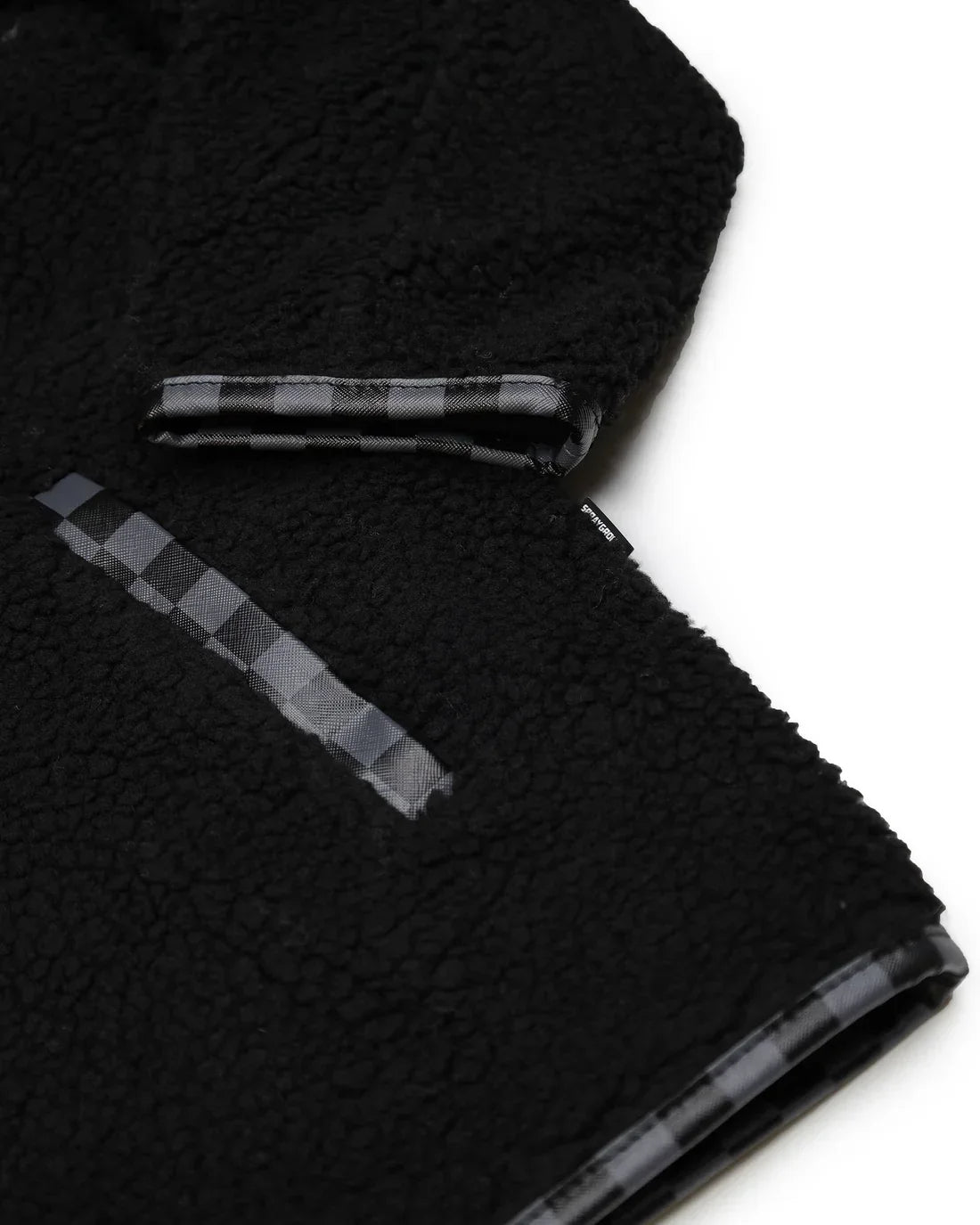 Dettaglio giacca teddy nera con inserti checkered, tessuto effetto peluche, stile casual.
