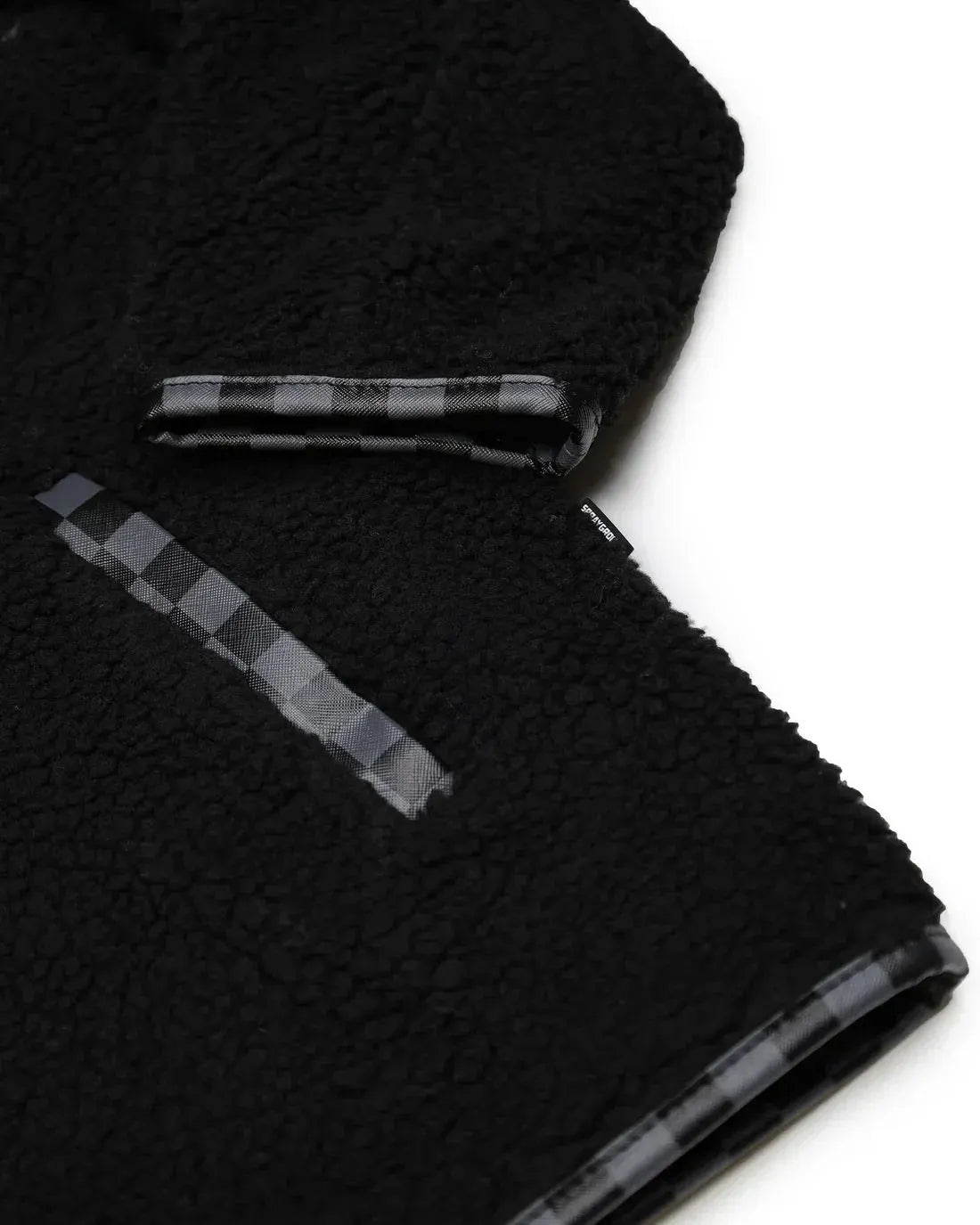 Dettaglio giacca teddy nera con inserti checkered, tessuto effetto peluche, stile casual.