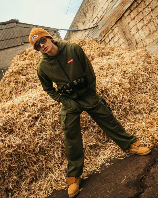 Uomo con felpa verde militare e pantaloni cargo, cappello arancione su sfondo rustico