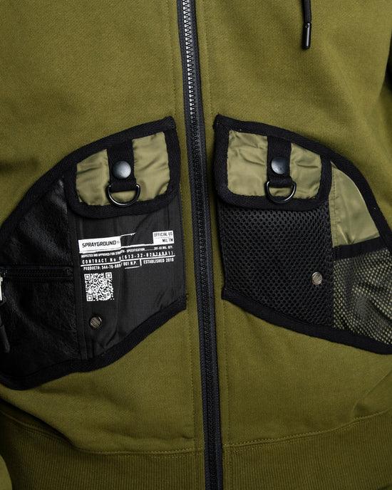 Dettaglio felpa verde con zip, tasche frontali multitasche nere e verde oliva, stile streetwear.