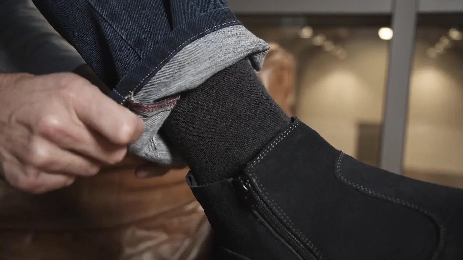 Dettaglio di mano che piega jeans sopra calza nera e stivaletto nero da uomo, moda elegante.