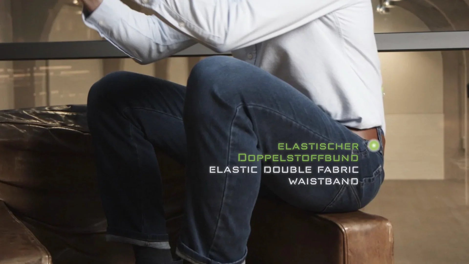Jeans uomo con cintura elasticizzata doppio tessuto, stile casual elegante, seduto su divano di pelle.
