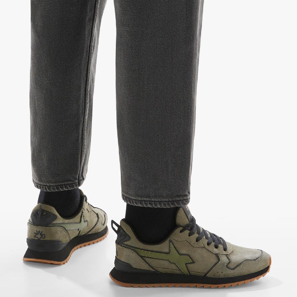 Sneaker uomo verde militare con suola nera e dettagli a contrasto, indossata con jeans scuri.