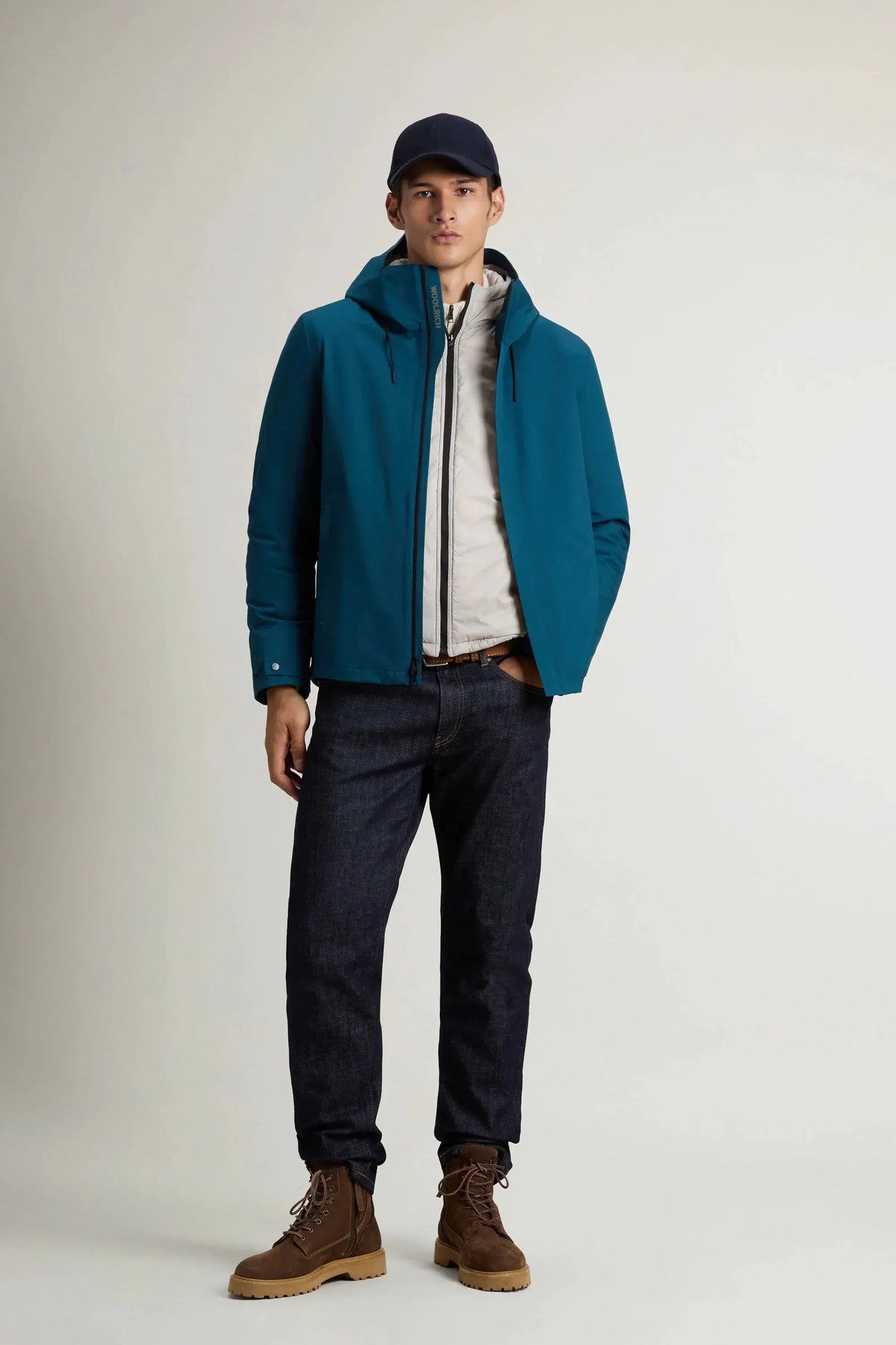 Uomo indossa giacca blu impermeabile con cappuccio, jeans e scarponcini marroni