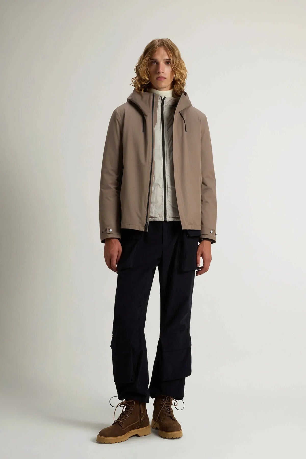 Uomo con giacca taupe 3-in-1, pantaloni cargo neri e scarponcini marroni, look casual.