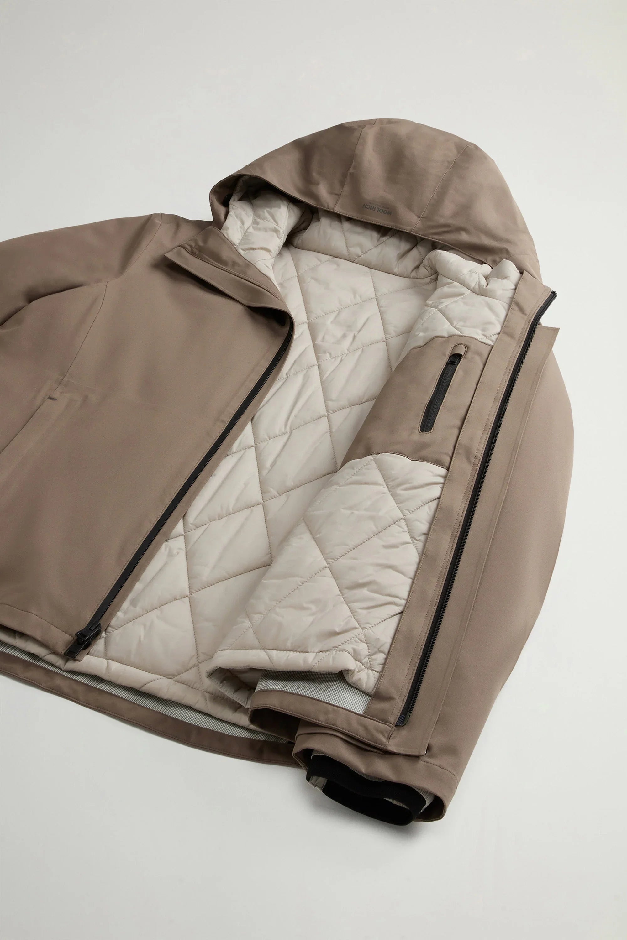 Giacca uomo beige con cappuccio e interno trapuntato, design sportivo e zip laterali.