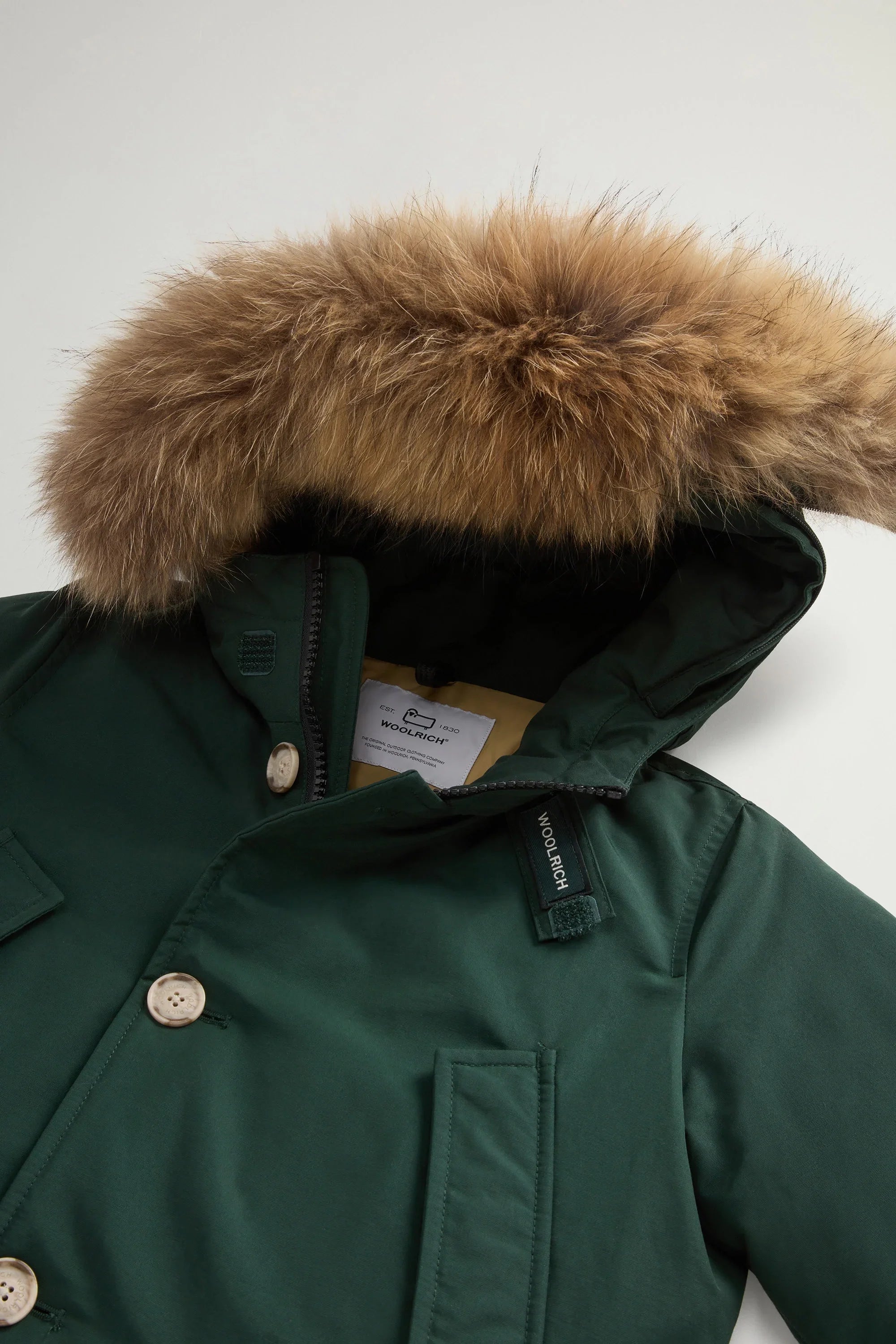 Parka verde scuro con cappuccio e pelliccia removibile, bottoni chiari, dettaglio label Woolrich