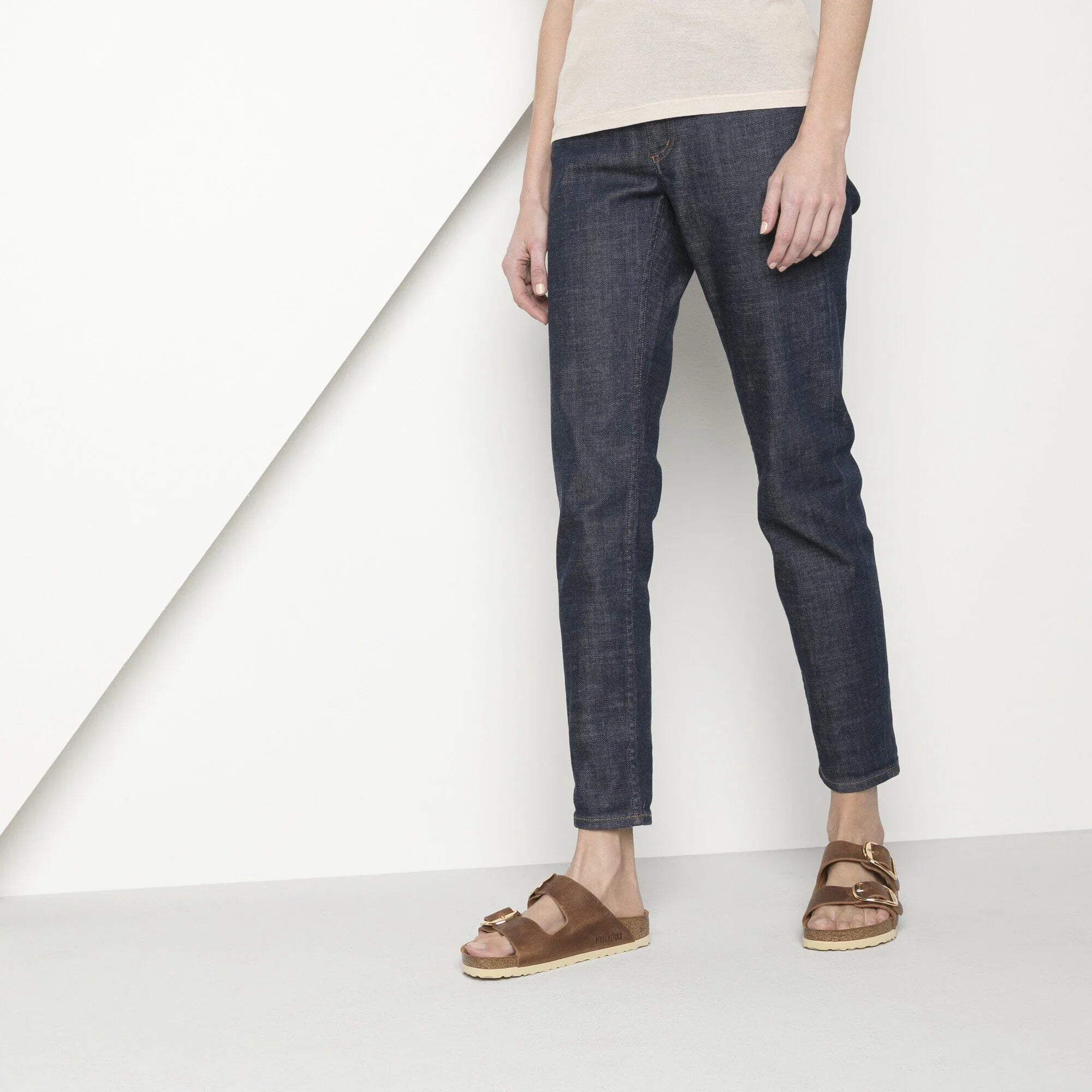 Donna con jeans slim fit blu scuro e sandali marroni in pelle, moda casual
