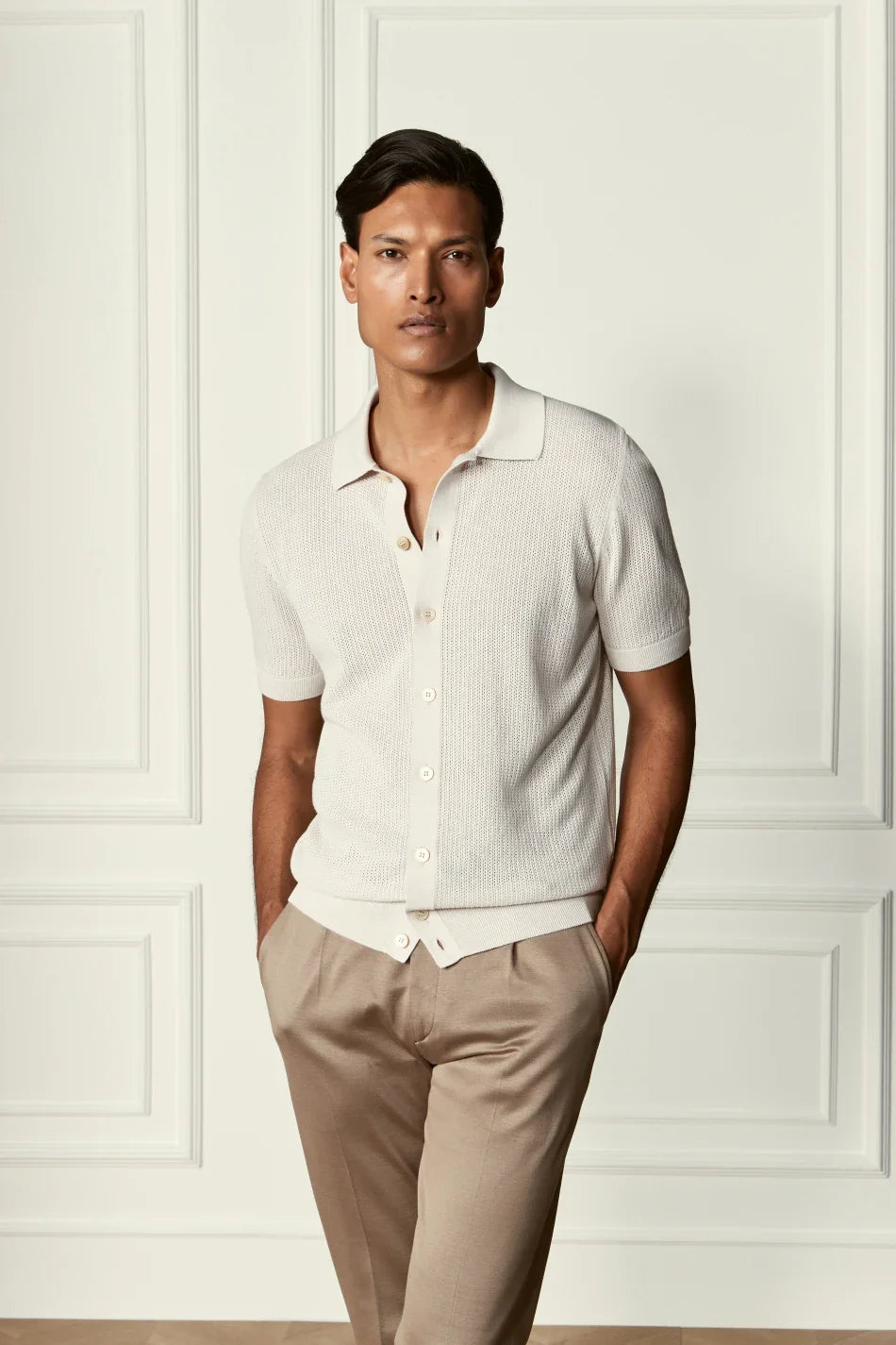 Modello uomo indossa polo beige a manica corta e pantaloni eleganti in un setting minimal elegante.