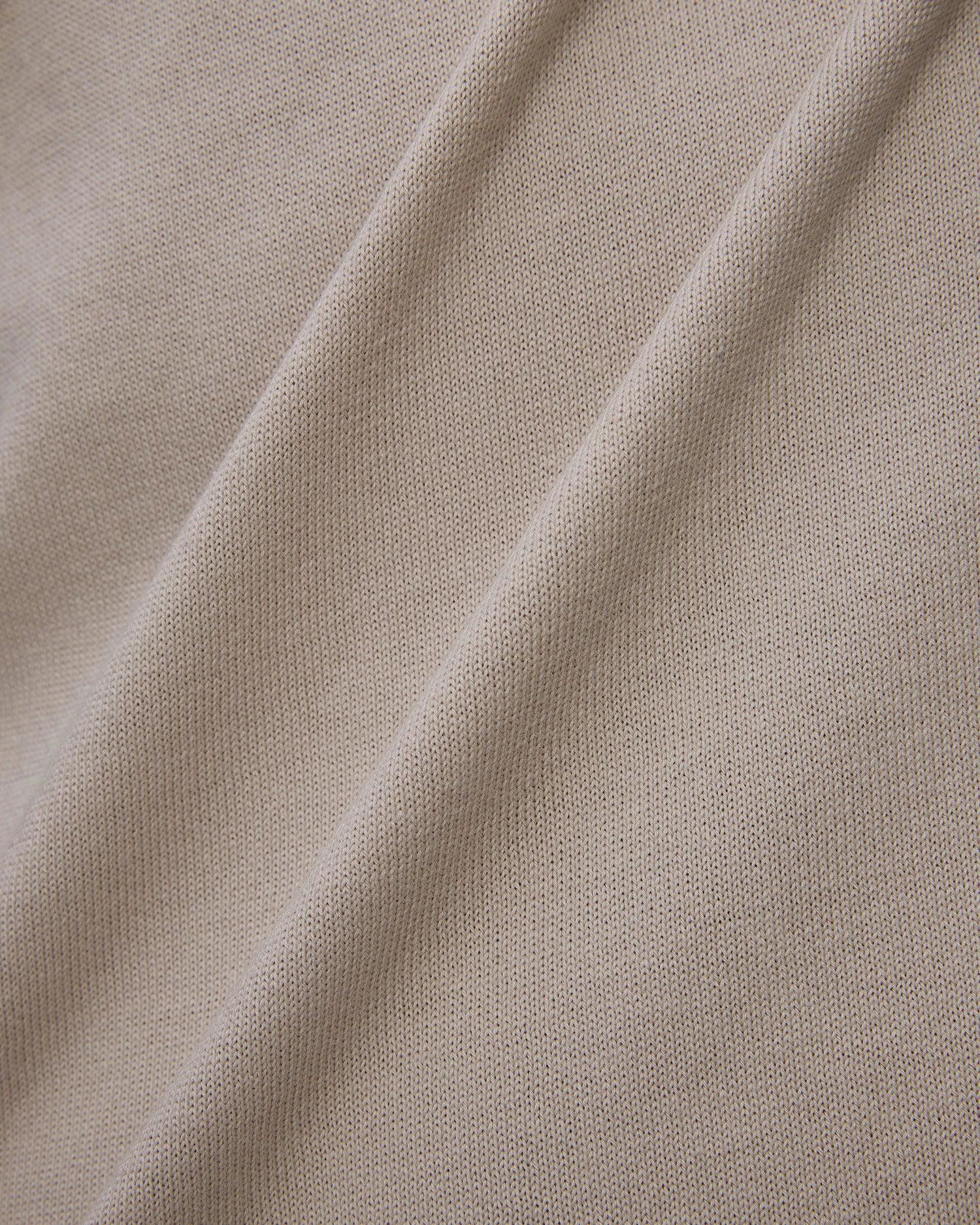 Dettaglio tessuto beige in maglia, texture morbida e pieghe naturali, abbigliamento elegante.