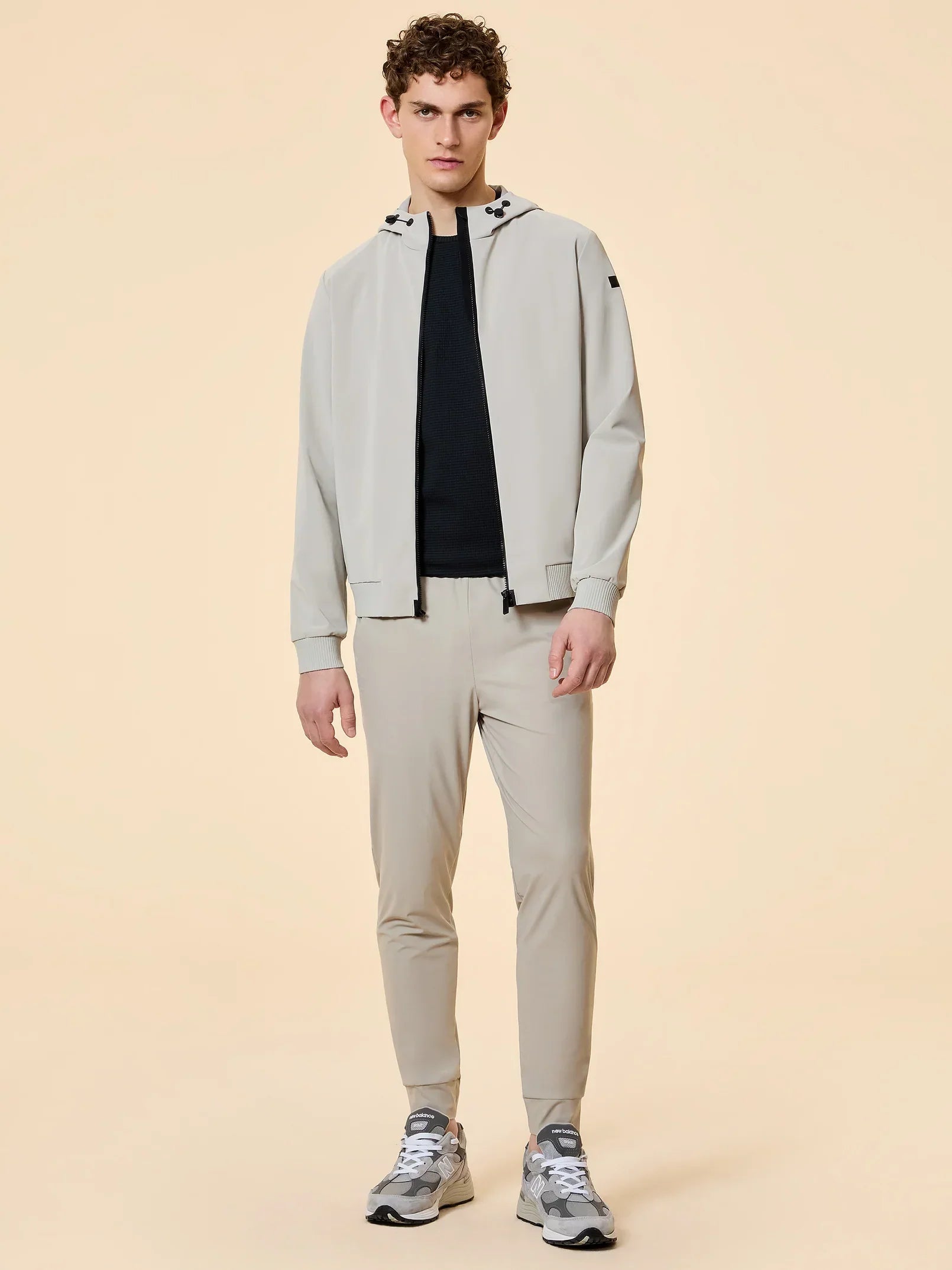 uomo con completo sportivo beige, giacca con cappuccio, pantaloni slim, sneakers grigie