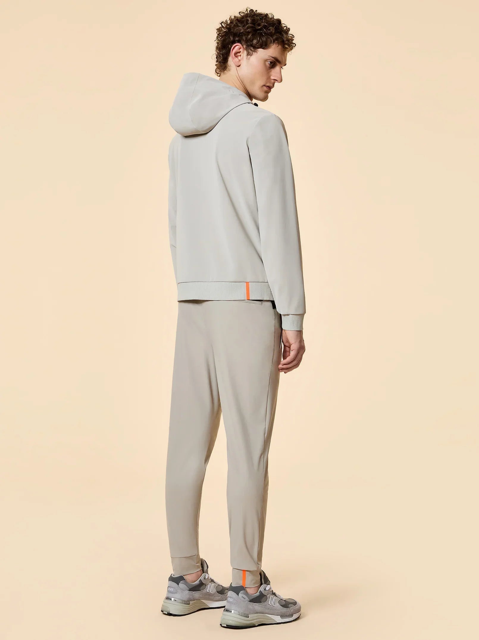 Modello uomo con tuta beige sportiva, felpa con cappuccio e pantaloni, sneakers grigie