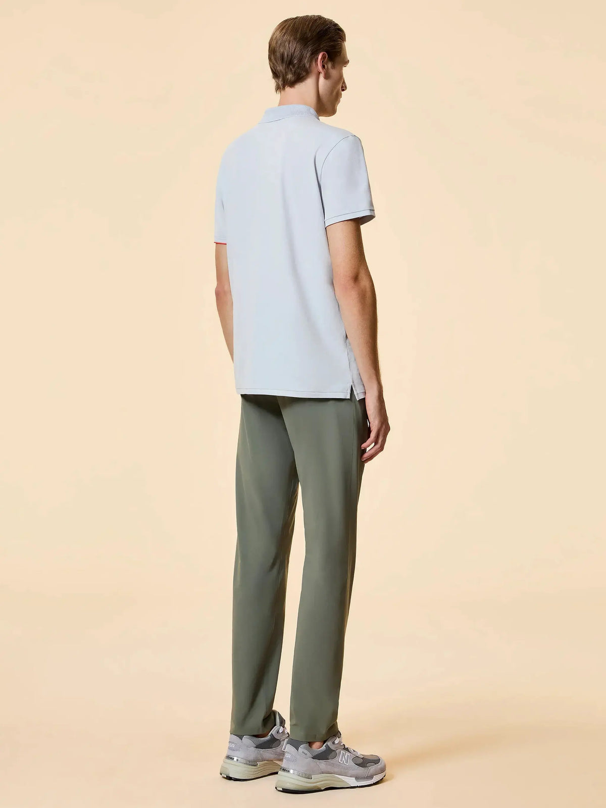 Uomo di spalle con polo a maniche corte chiara, pantaloni verde oliva e sneakers grigie