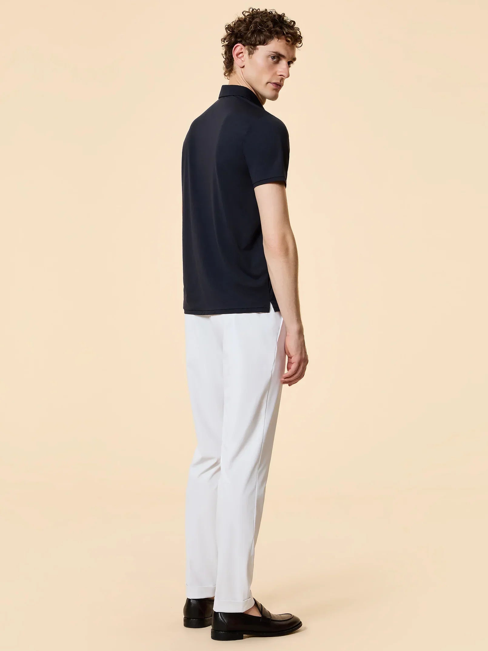 Uomo con polo blu scuro e pantaloni bianchi eleganti, vista posteriore, moda uomo