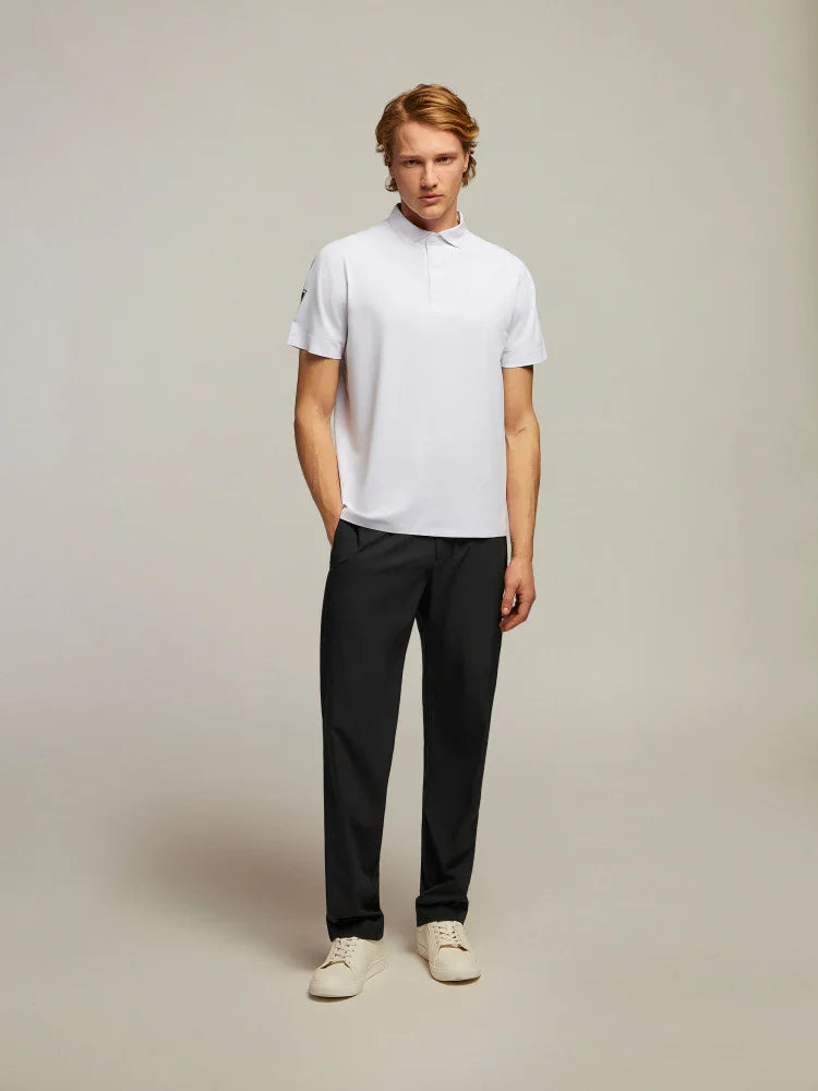 Modello uomo con polo bianca, pantaloni neri eleganti e sneakers chiare su sfondo neutro.