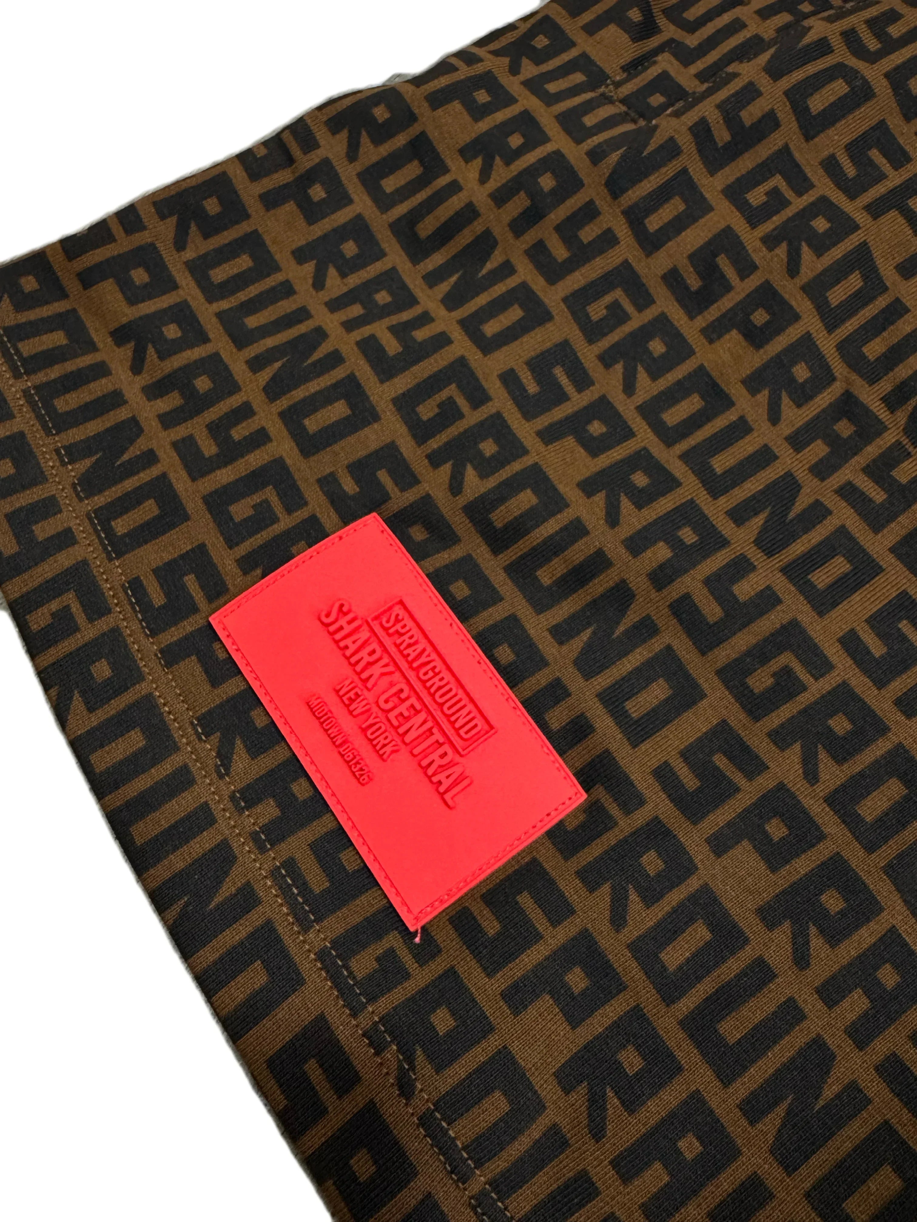 Dettaglio pantalone marrone con stampa logata nera e patch rossa Sprayground in rilievo.