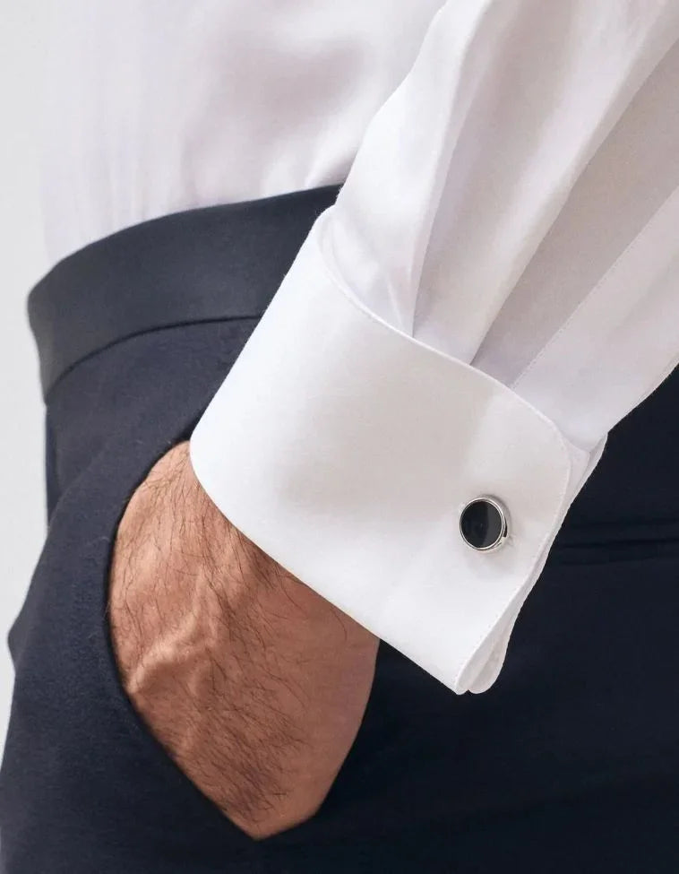 Polso di camicia bianca elegante da uomo con gemello nero, mano in tasca pantaloni scuri