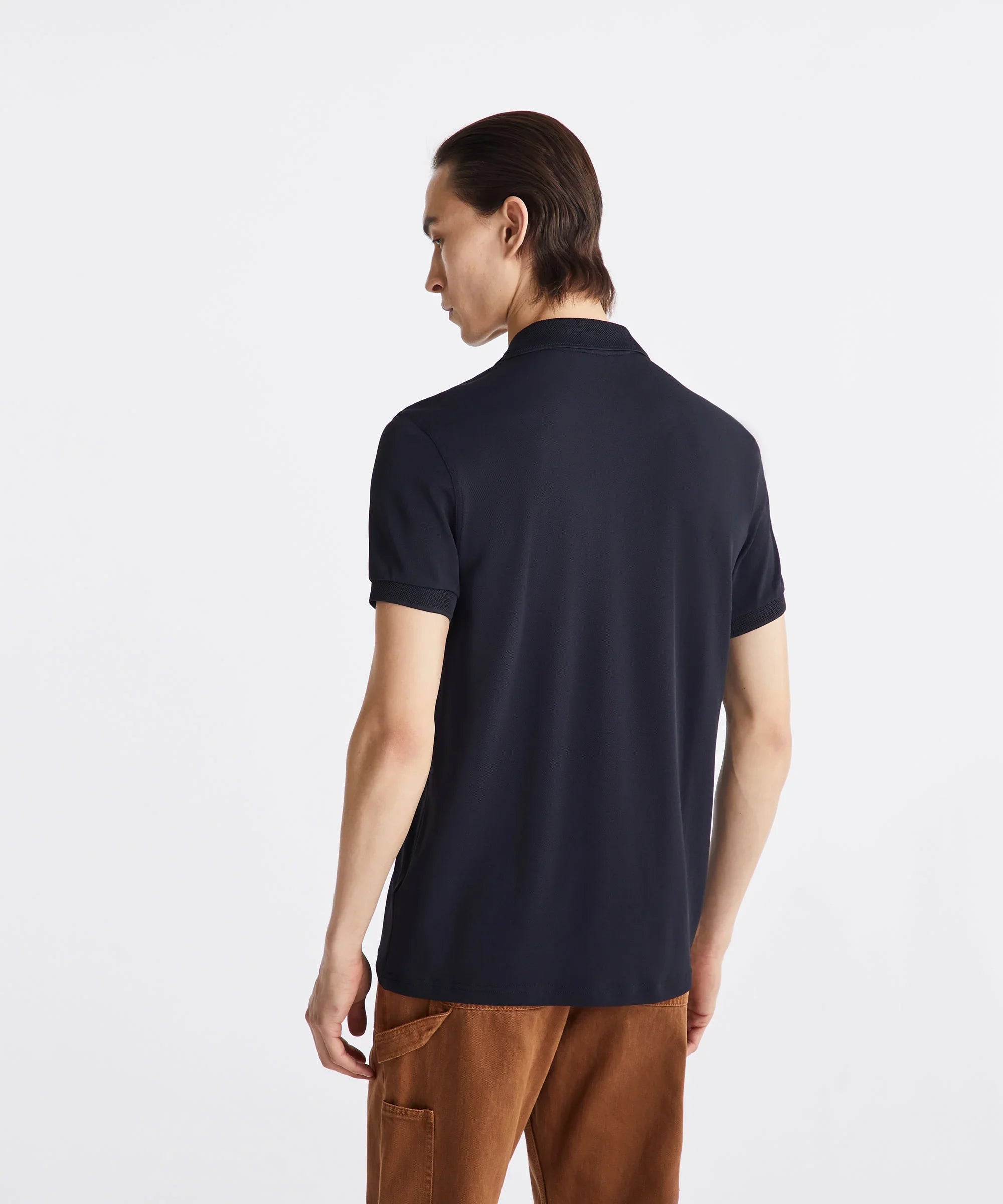 Uomo di spalle con polo nera manica corta e pantaloni marroni, moda uomo casual elegante.
