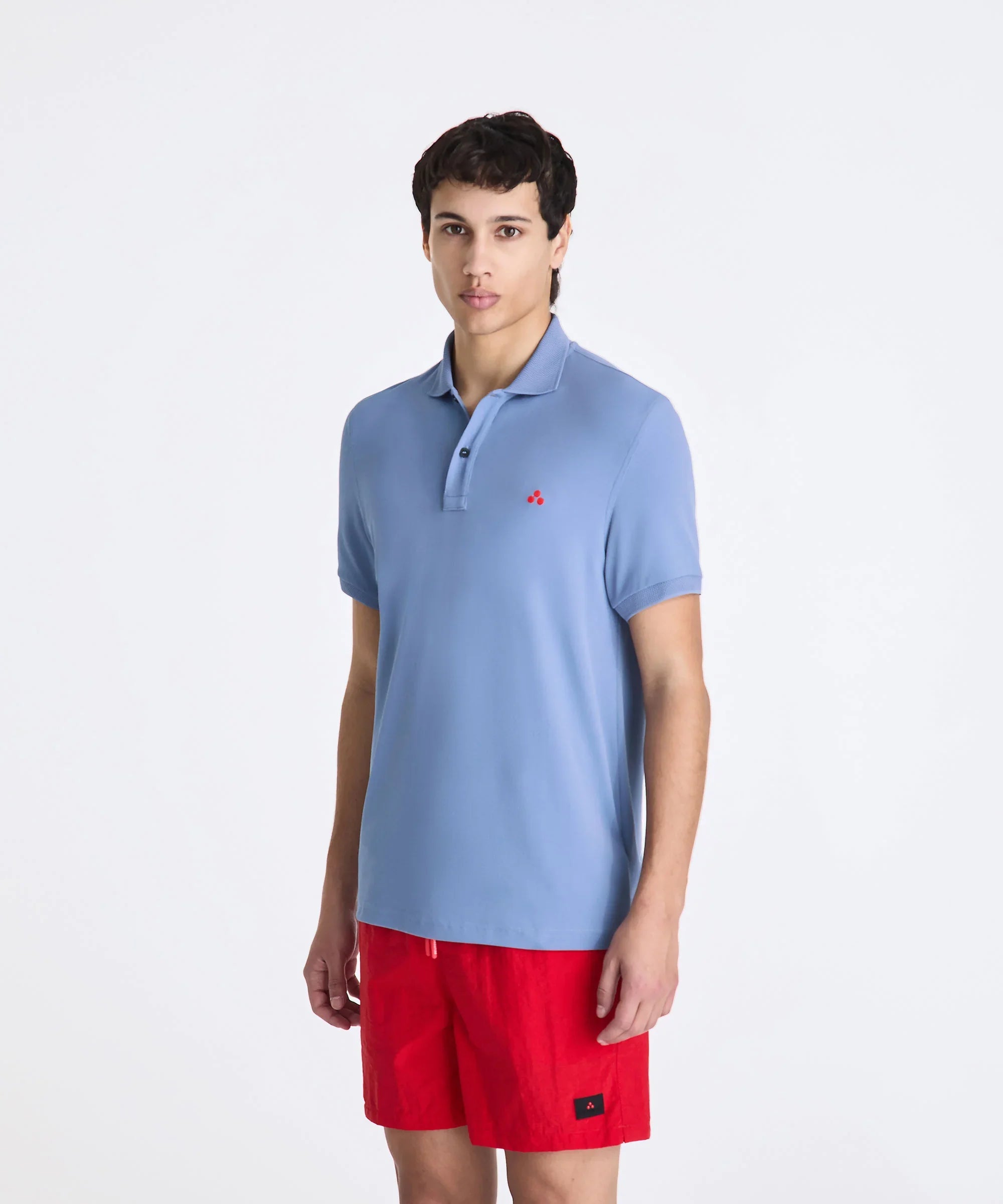 Modello indossa polo azzurra con logo rosso e pantaloncini rossi, moda uomo estiva.